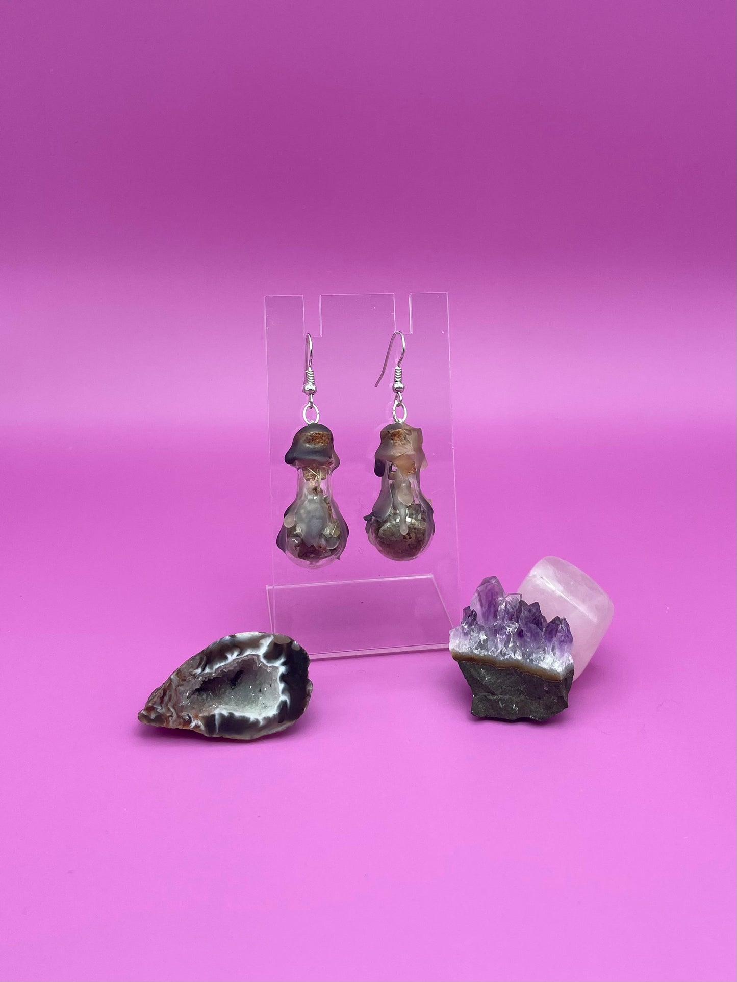 Protection spell earrings on clear stand with purple background
