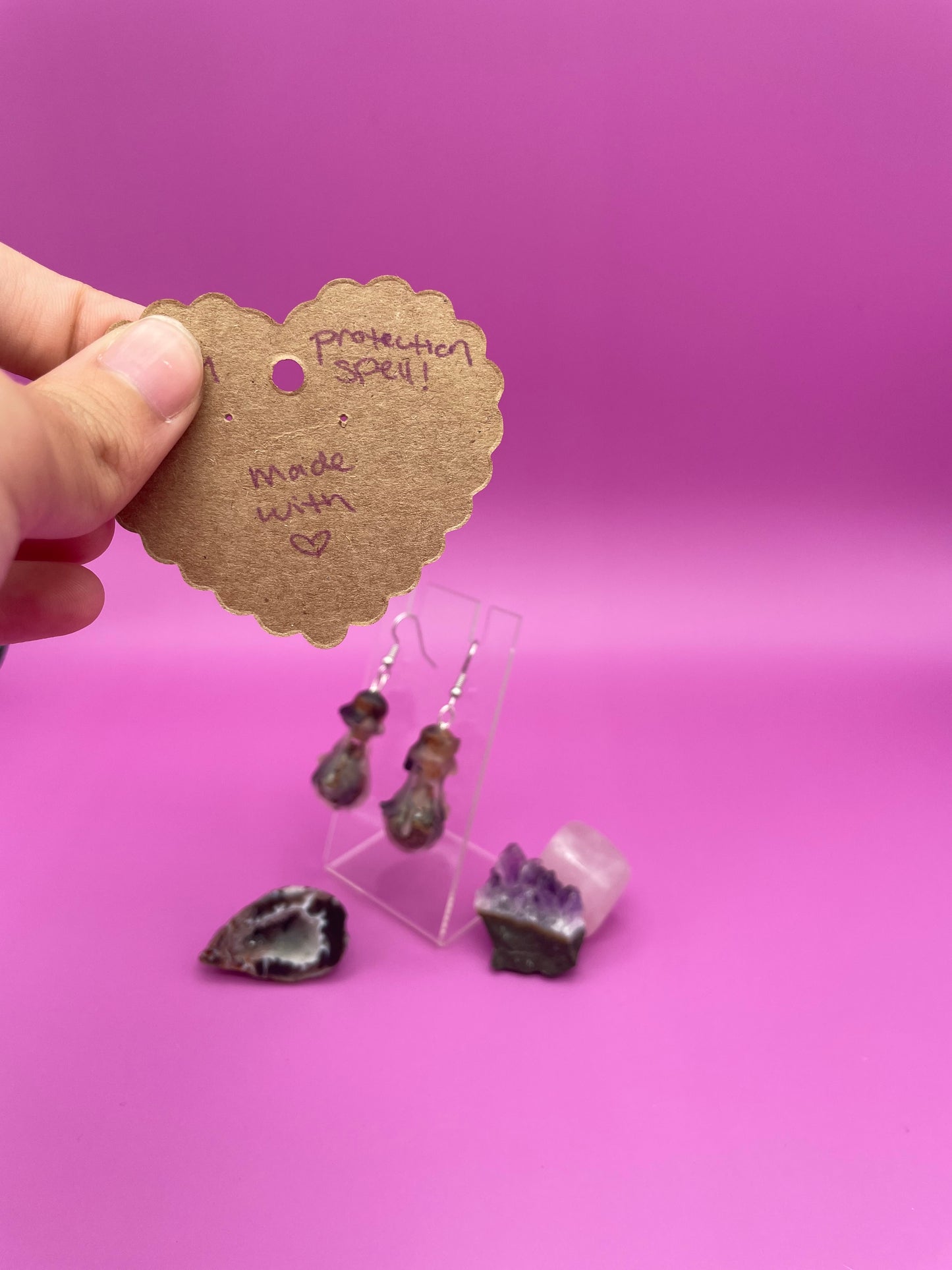 Protection spell earrings on clear stand with purple background