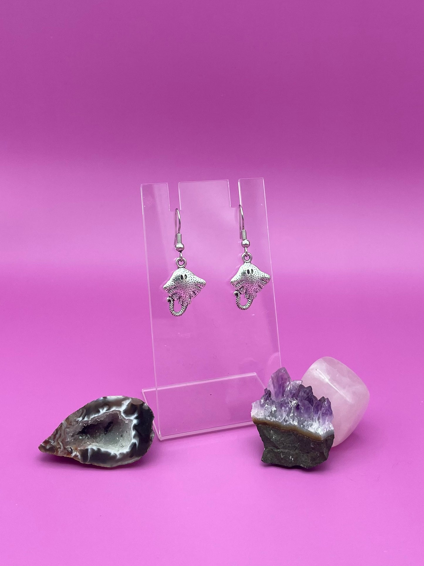 Silver stingray earrings on clear stand purple background