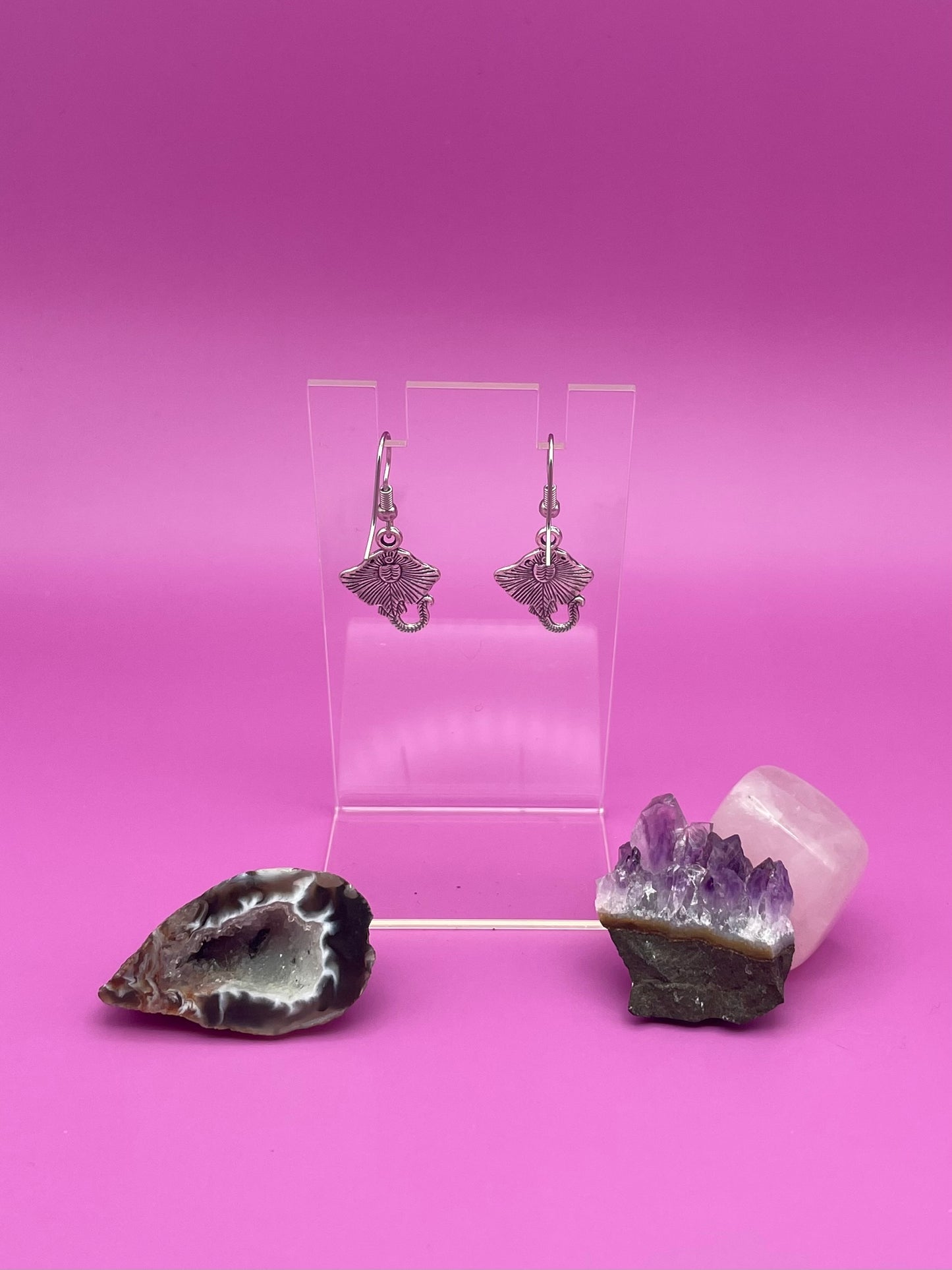 Silver stingray earrings on clear stand purple background