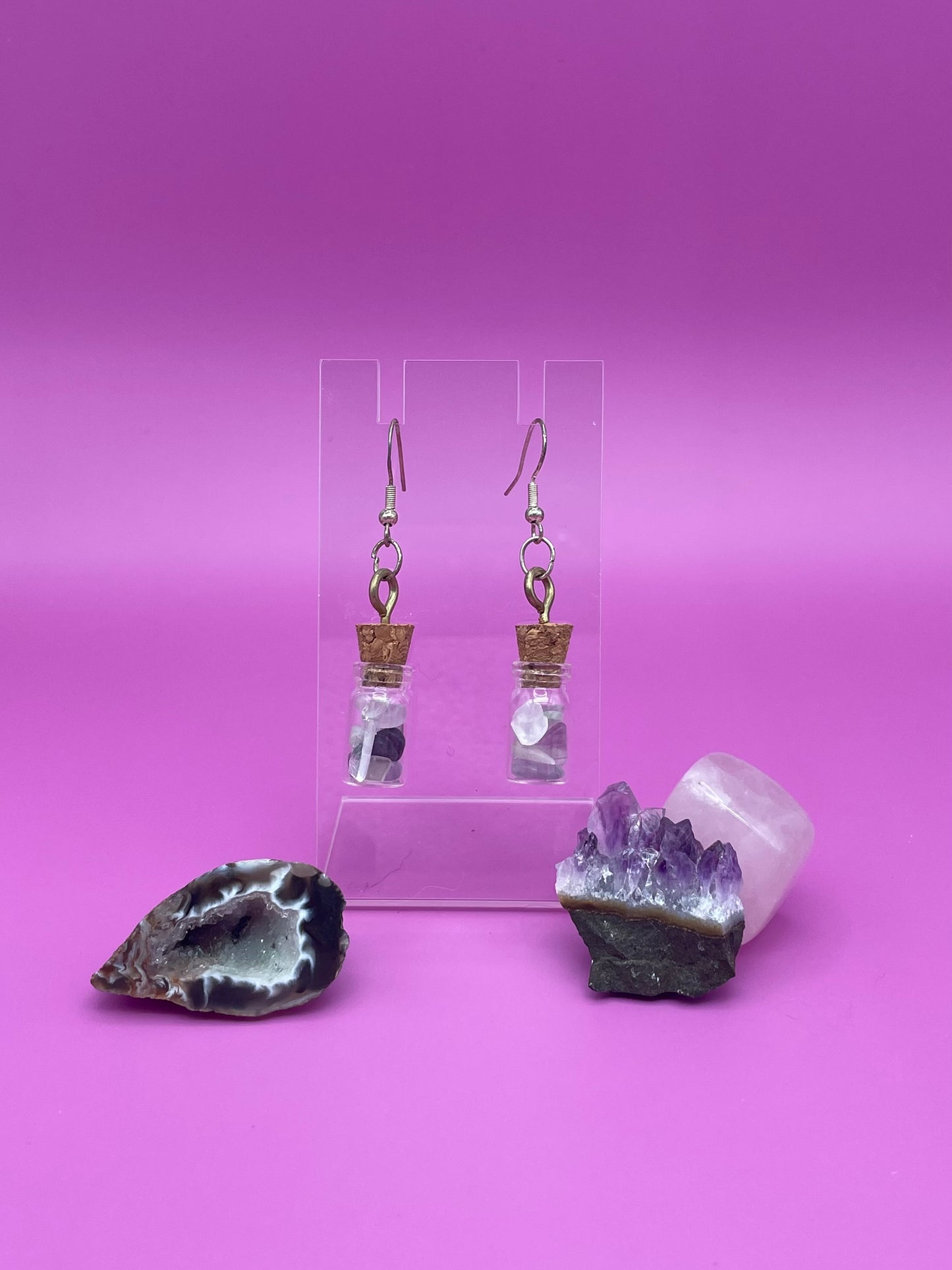 Fluorite filled jar earrings on a clear stand with crystals on a pink background