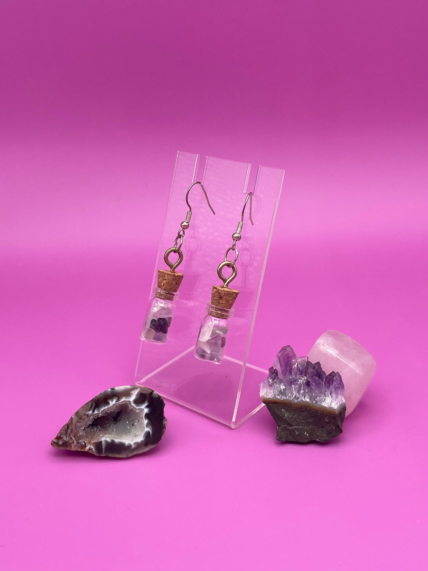 Fluorite filled jar earrings on a clear stand with crystals on a pink background