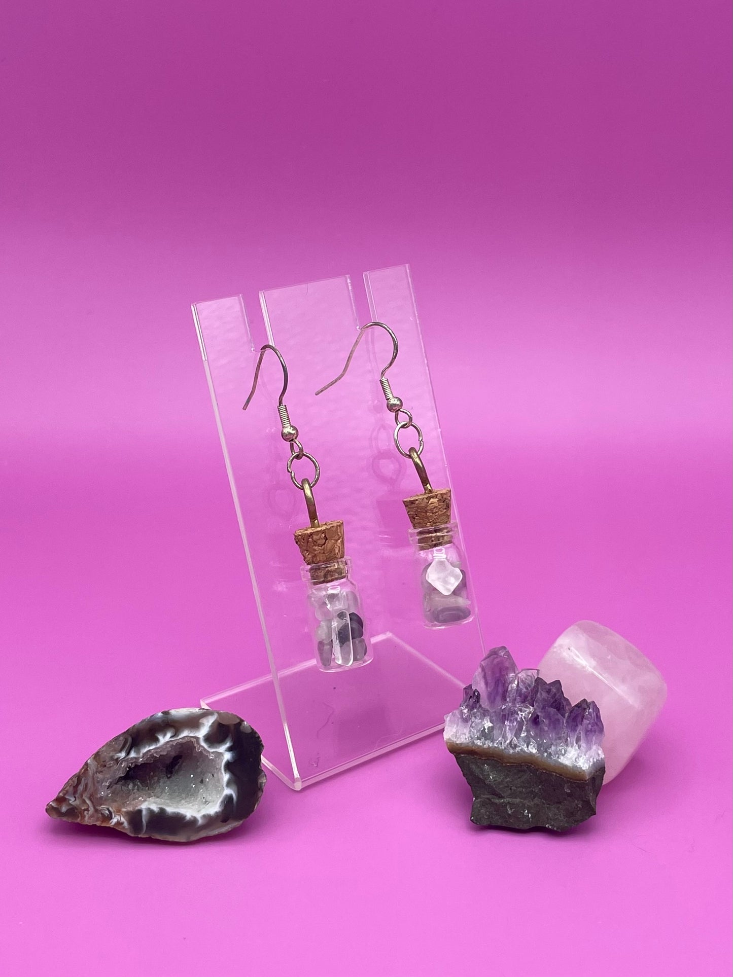 Fluorite filled jar earrings on a clear stand with crystals on a pink background