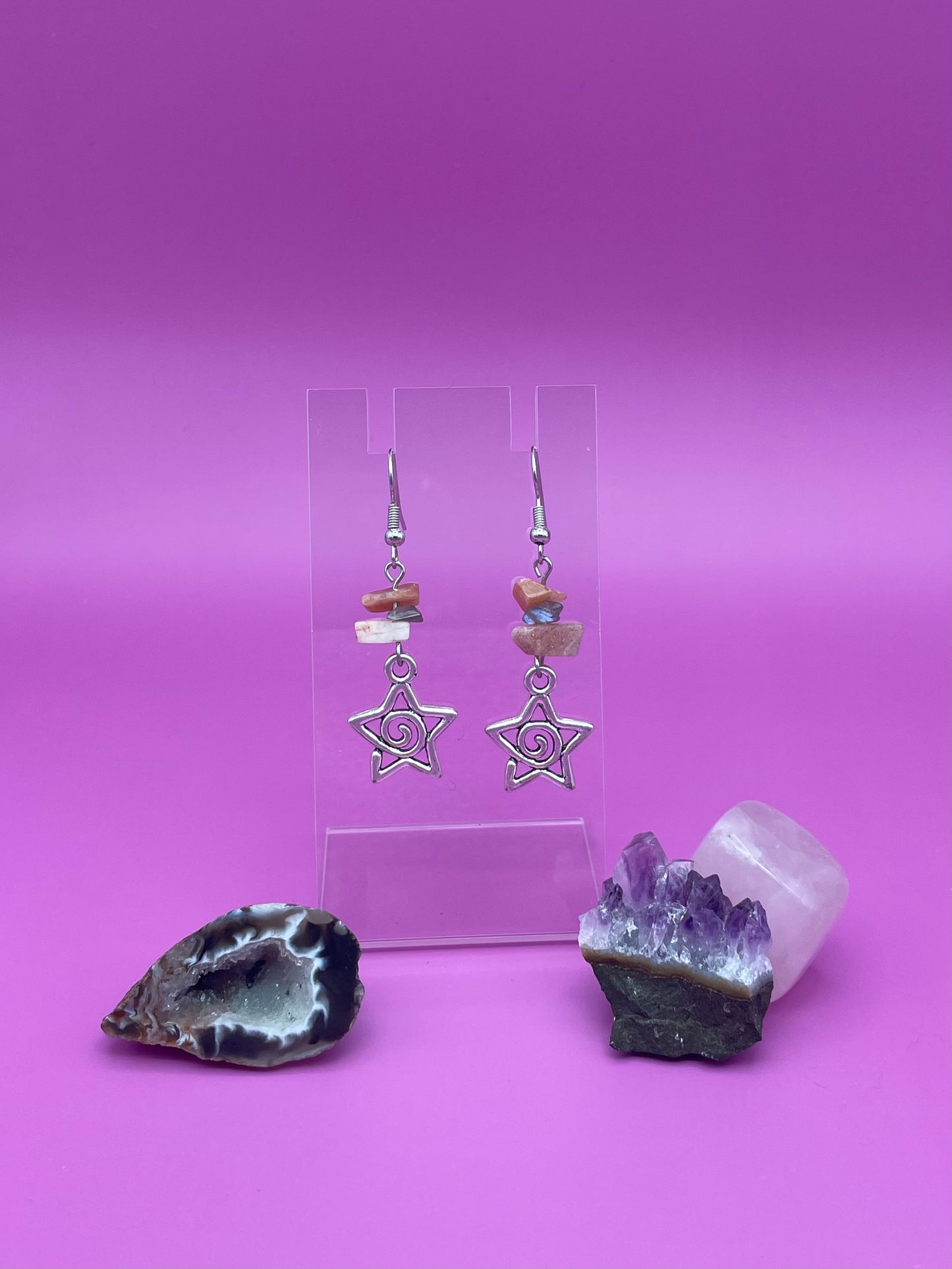 Star-shaped swirl earrings on a clear stand with amethyst crystal and a purple background