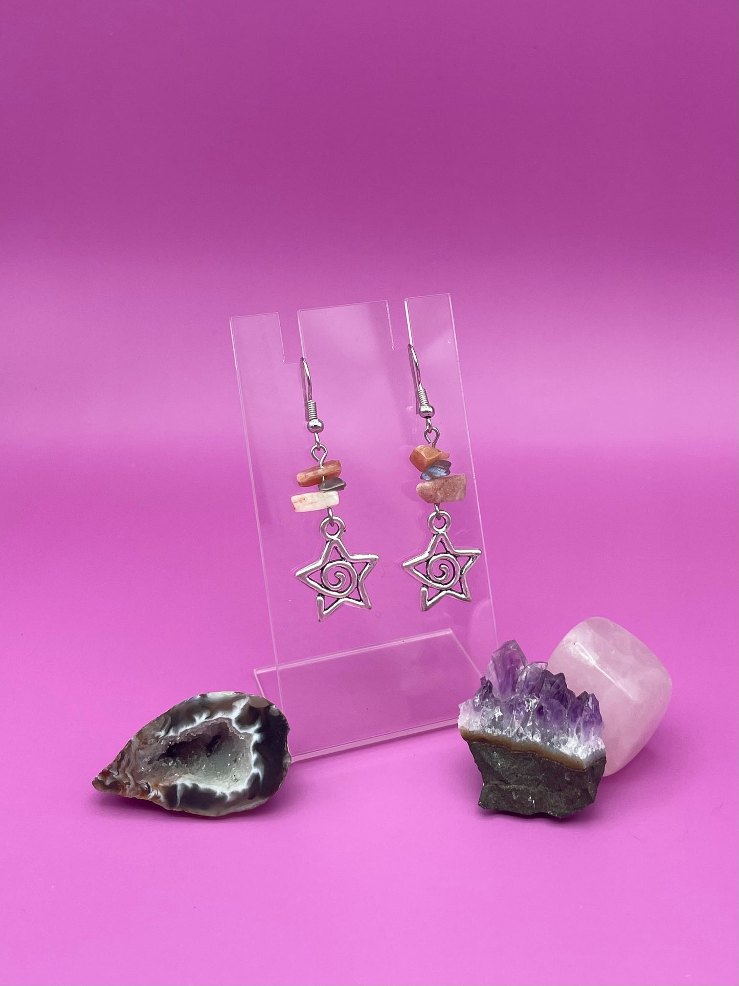 Star-shaped swirl earrings on a clear stand with amethyst crystal and a purple background