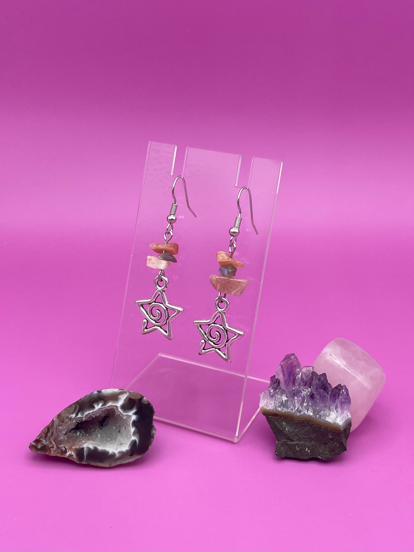 Star-shaped swirl earrings on a clear stand with amethyst crystal and a purple background