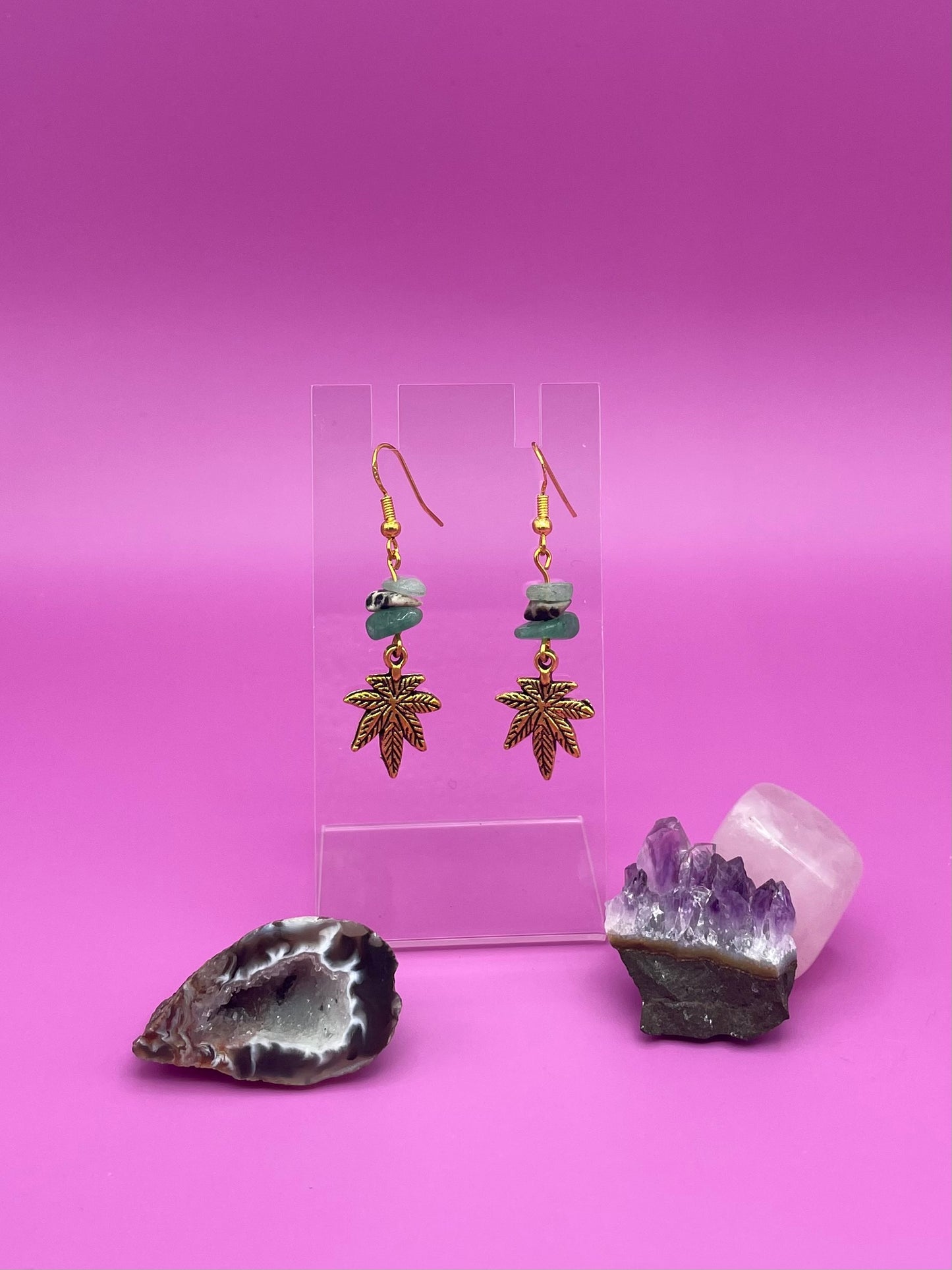 Gold leaf charm with crystal chips earrings on a clear stand with amethyst crystal on a pink background