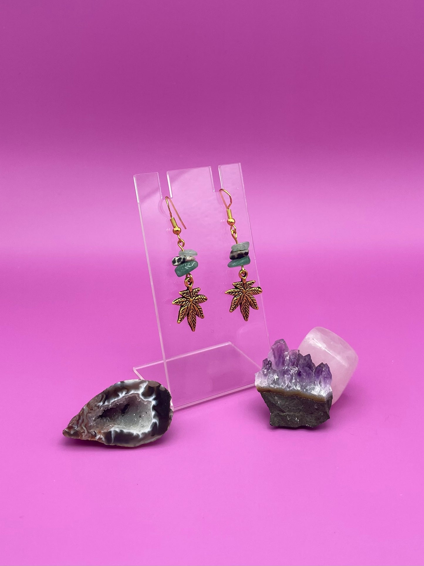 Gold leaf charm with crystal chips earrings on a clear stand with amethyst crystal on a pink background