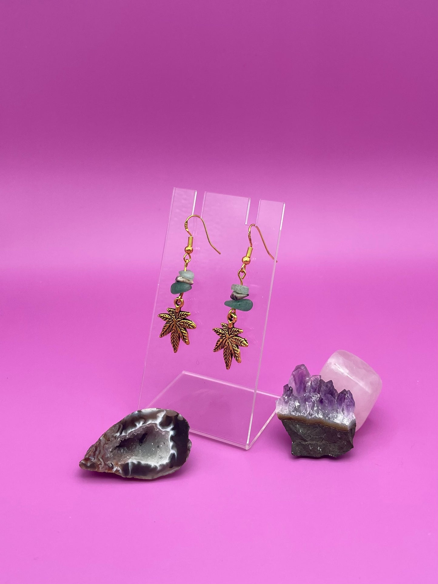 Gold leaf charm with crystal chips earrings on a clear stand with amethyst crystal on a pink background