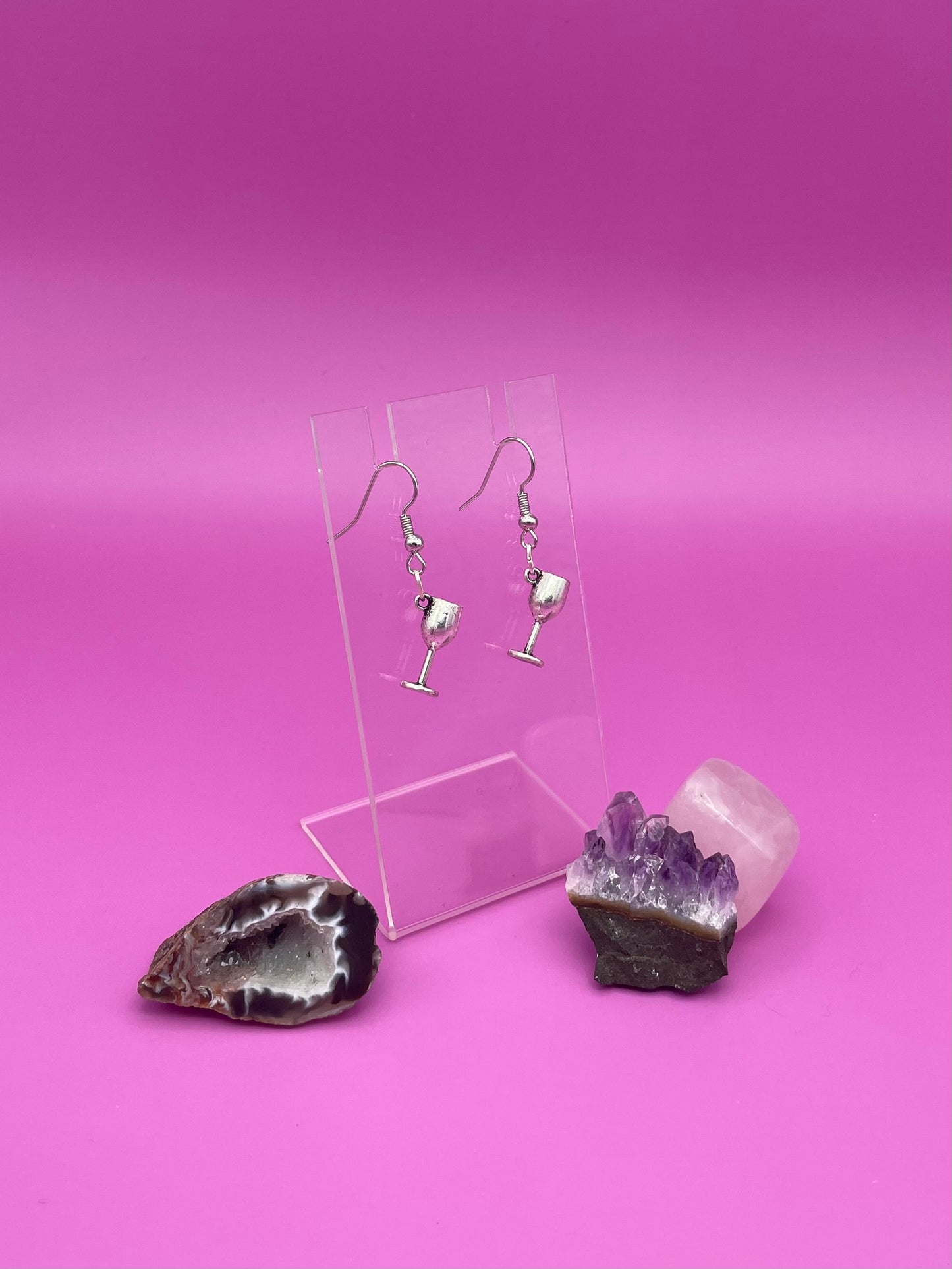 Silver wine glass earrings on a clear stand with purple background