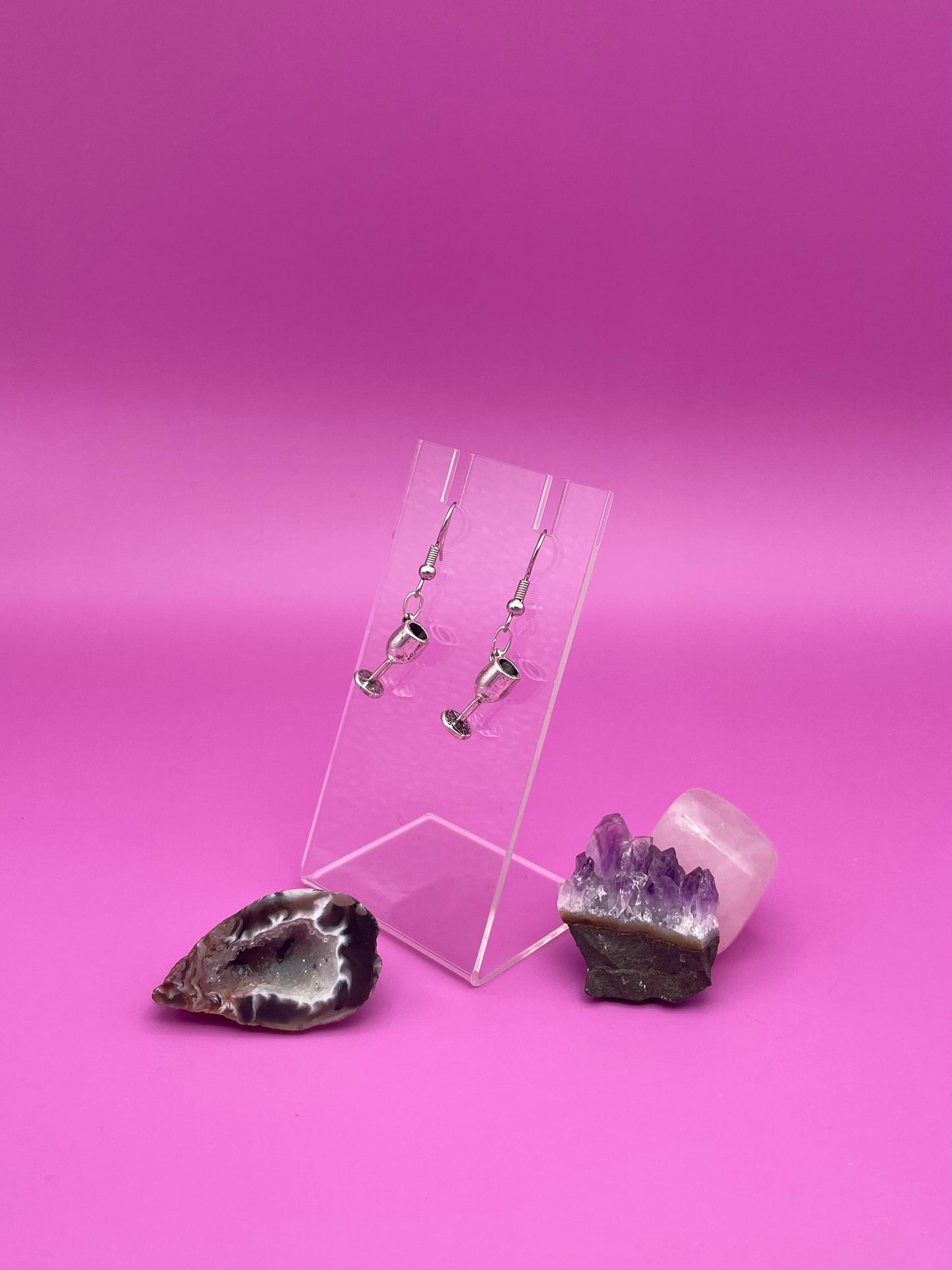 Silver wine glass earrings on a clear stand with purple background