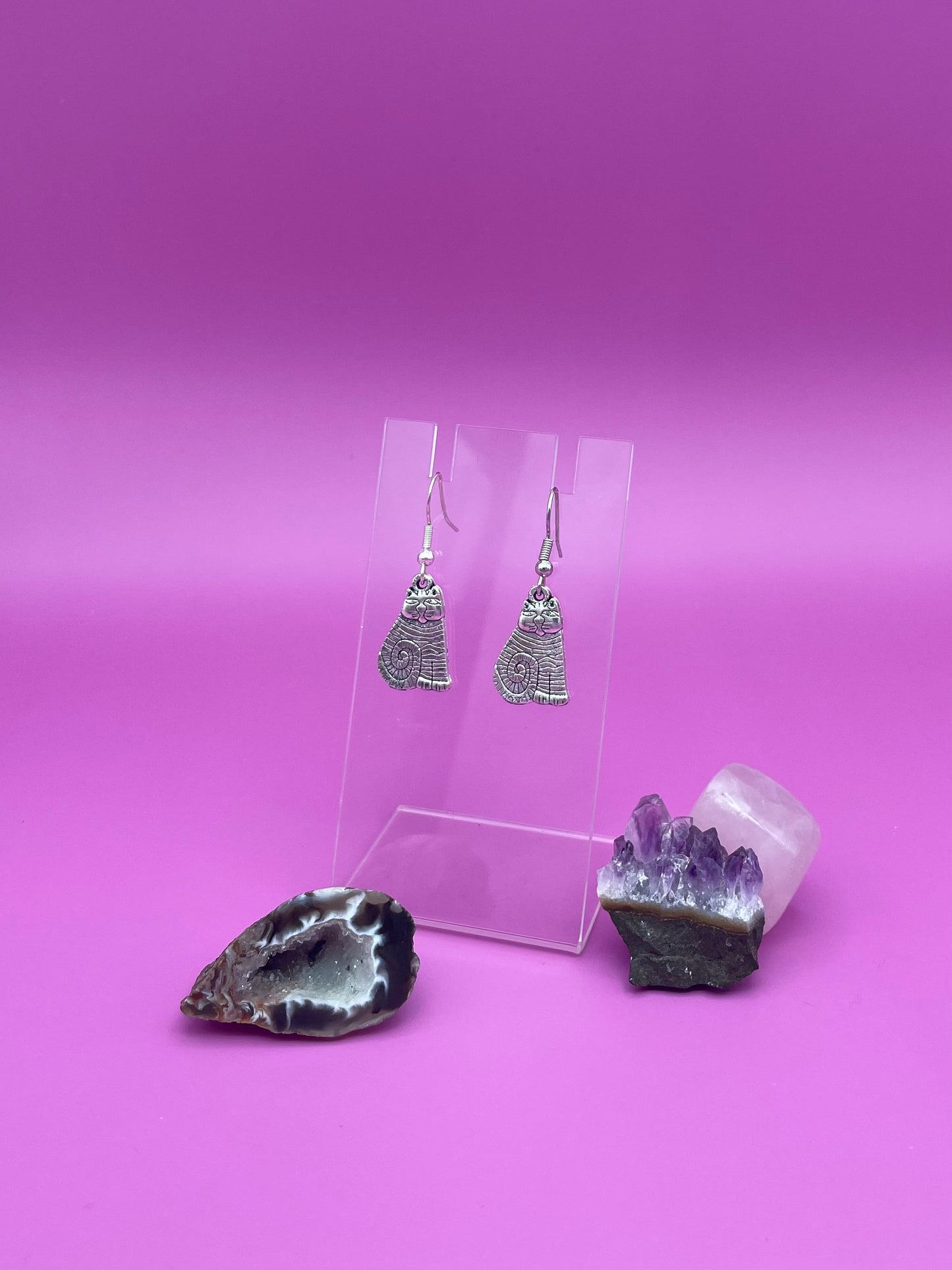 Silver cat earrings on a clear stand with purple background