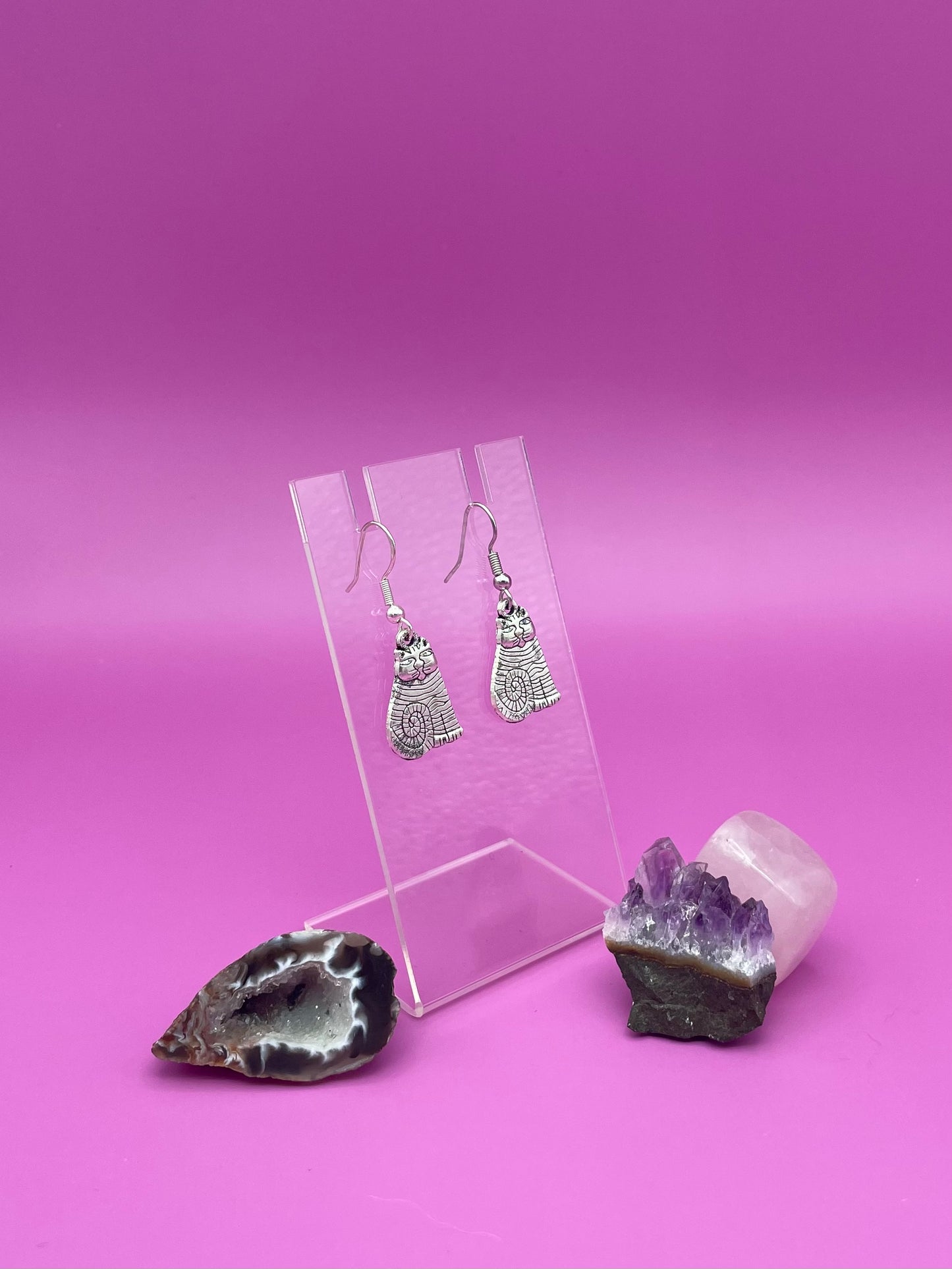 Silver cat earrings on a clear stand with purple background