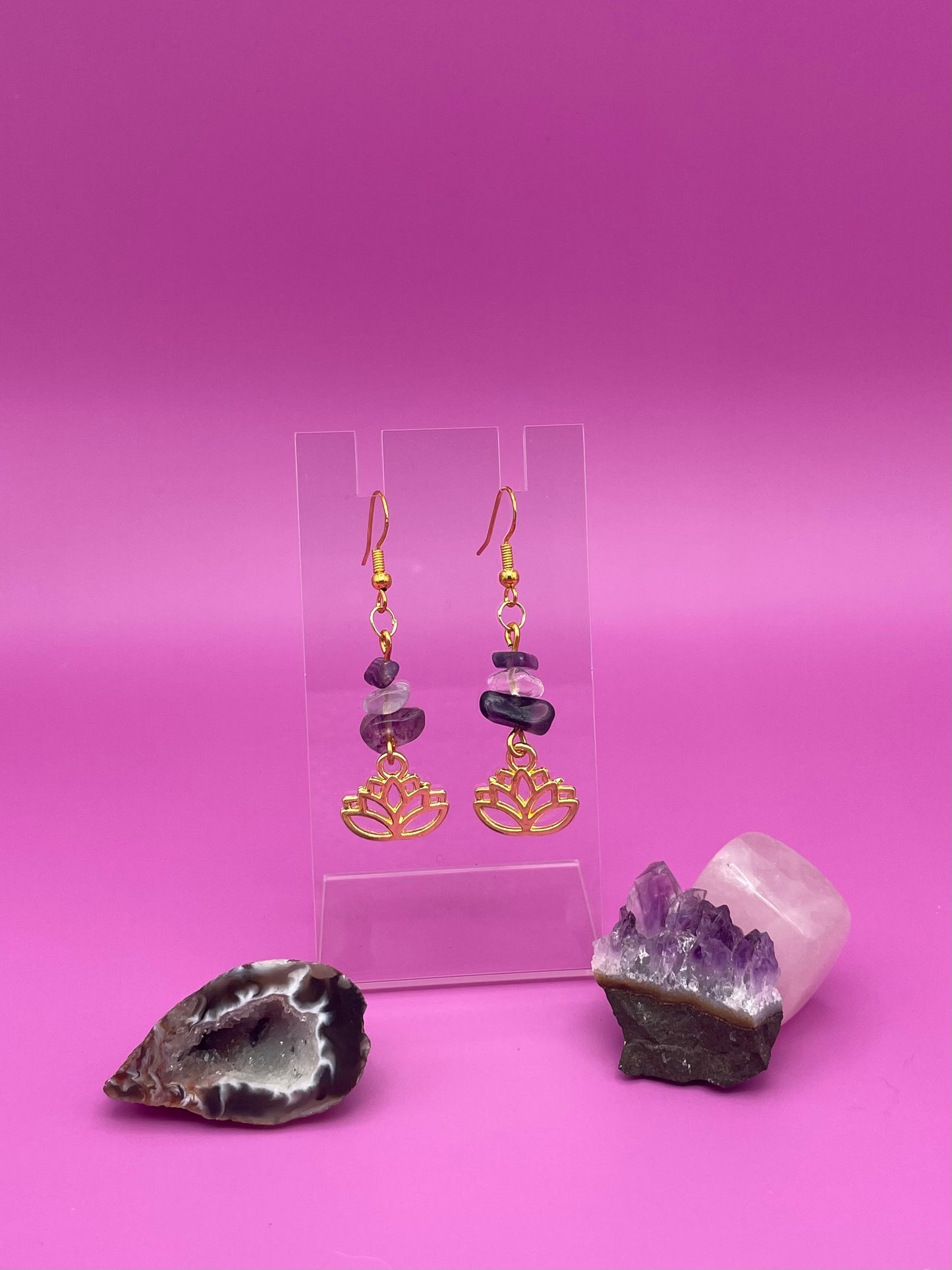 Gold lotus flower earrings with fluorite and clear quartz crystal chips on a clear stand with purple background
