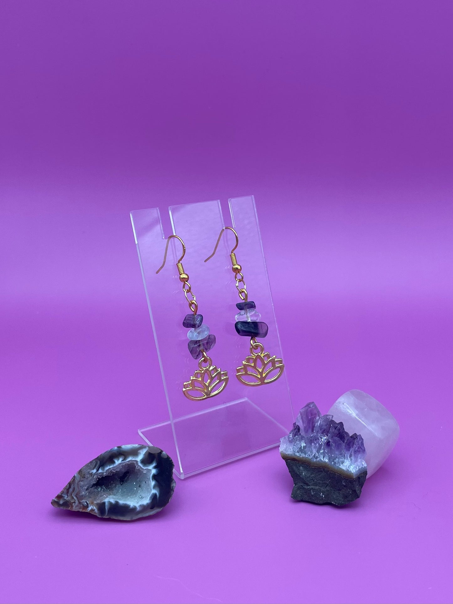 Gold lotus flower earrings with fluorite and clear quartz crystal chips on a clear stand with purple background