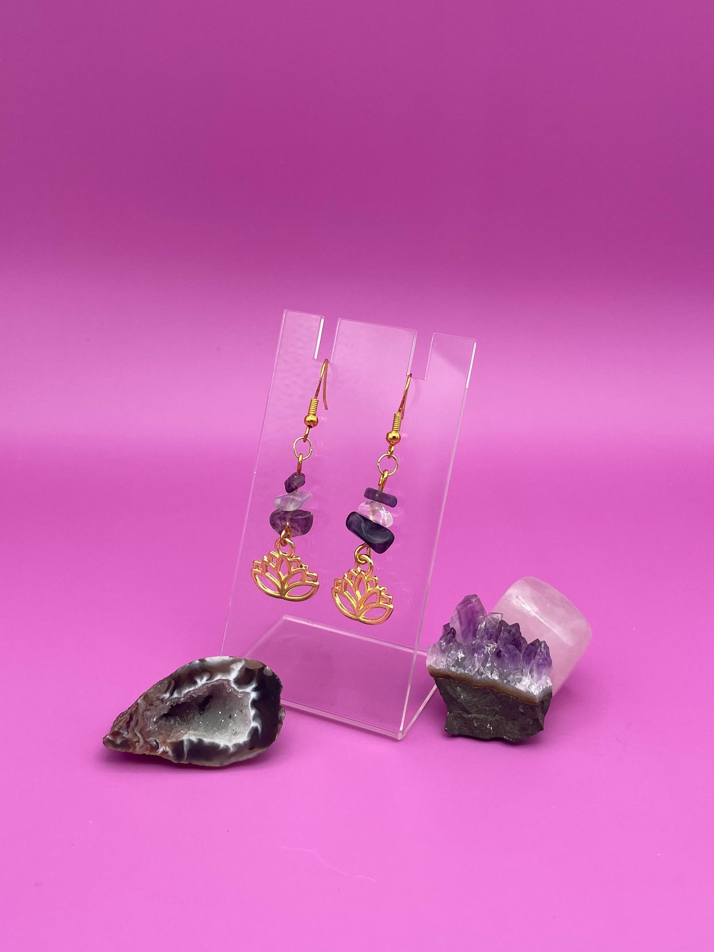 Gold lotus flower earrings with fluorite and clear quartz crystal chips on a clear stand with purple background