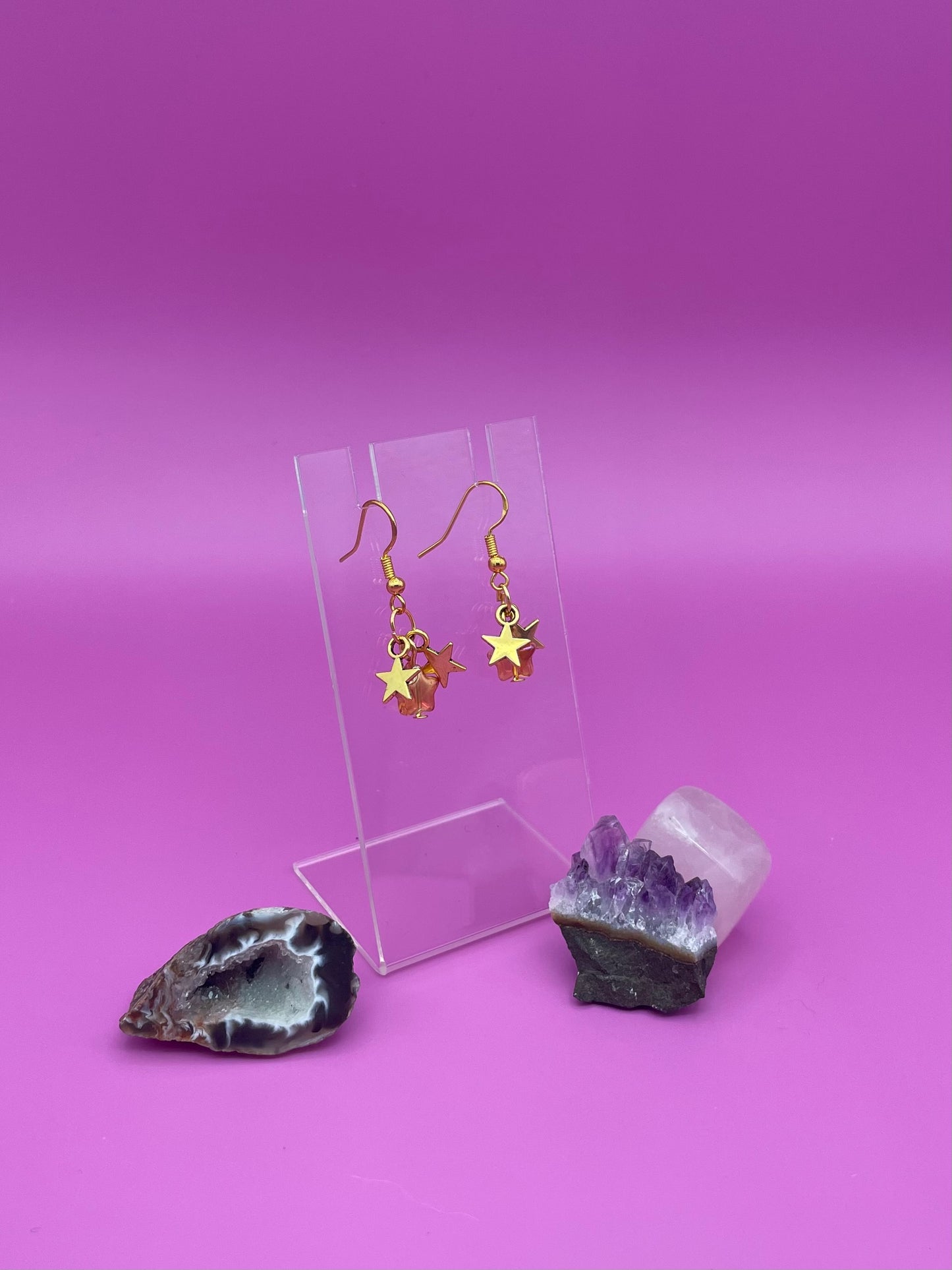 Three dangling stars earrings on a clear stand with crystals on a pink background