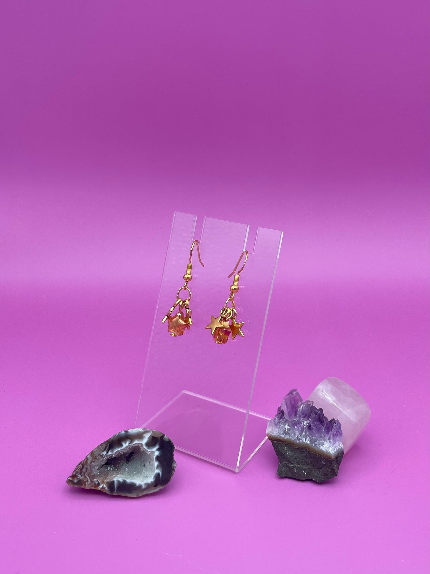 Three dangling stars earrings on a clear stand with crystals on a pink background