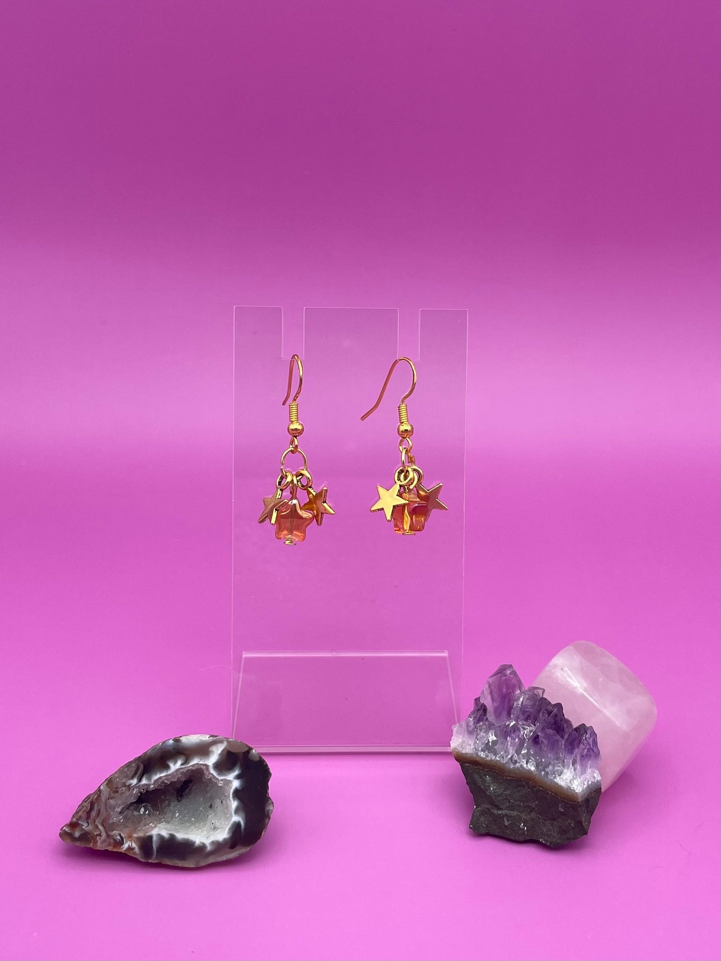 Three dangling stars earrings on a clear stand with crystals on a pink background