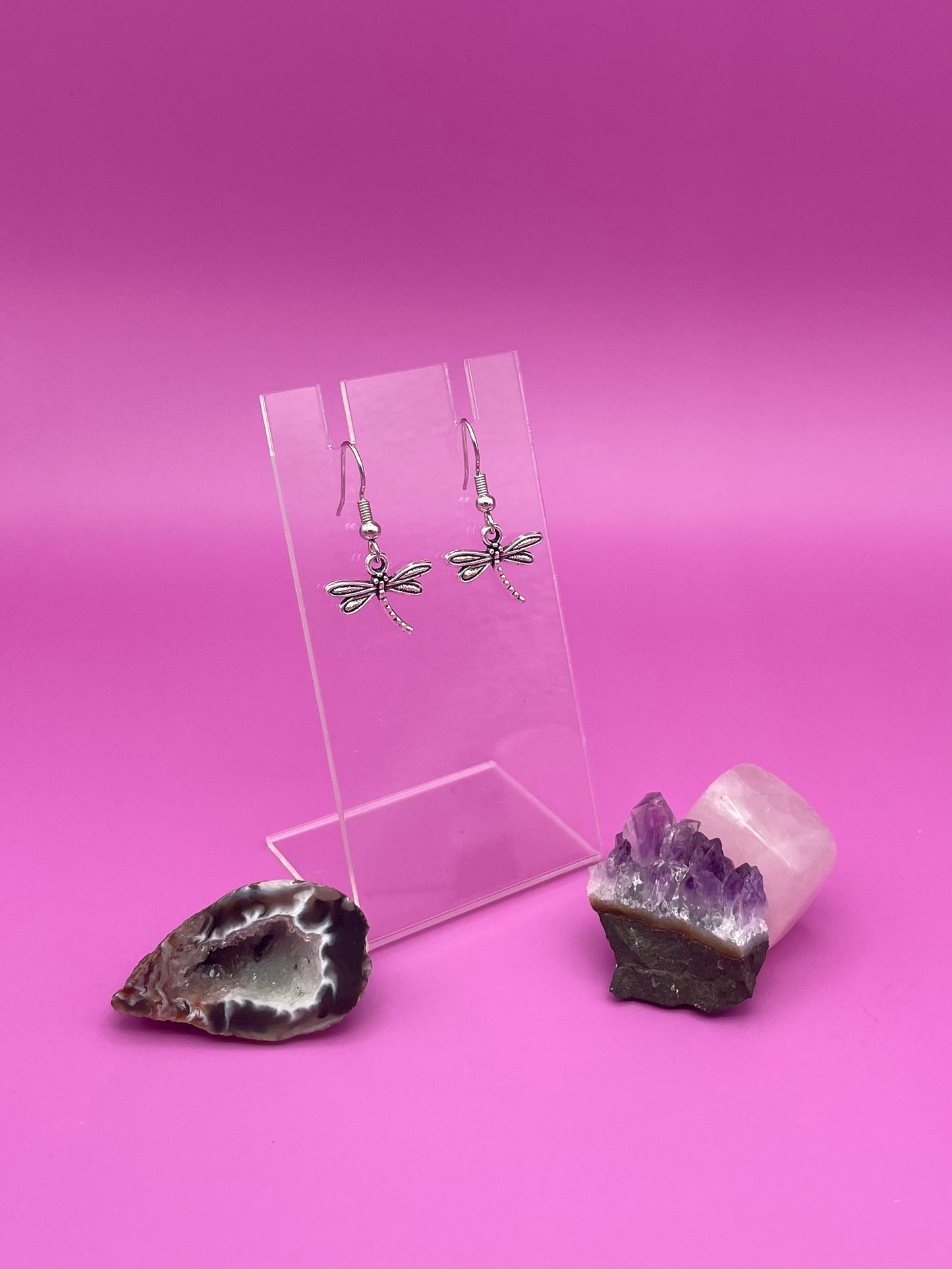 Dragonfly-shaped silver earrings on a clear stand with purple background