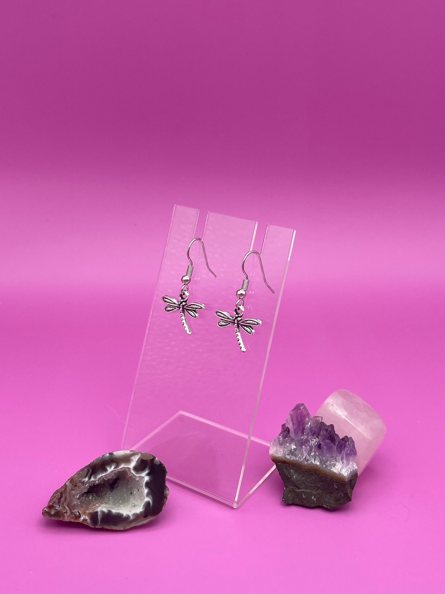 Dragonfly-shaped silver earrings on a clear stand with purple background