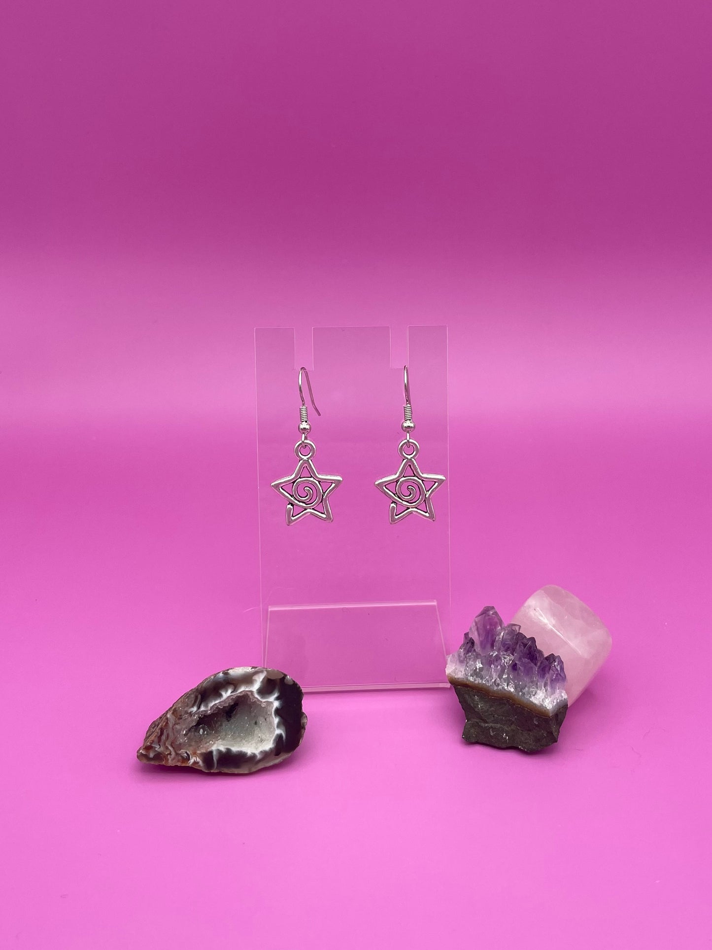Silver Star-shaped swirl earrings on a clear stand with purple background