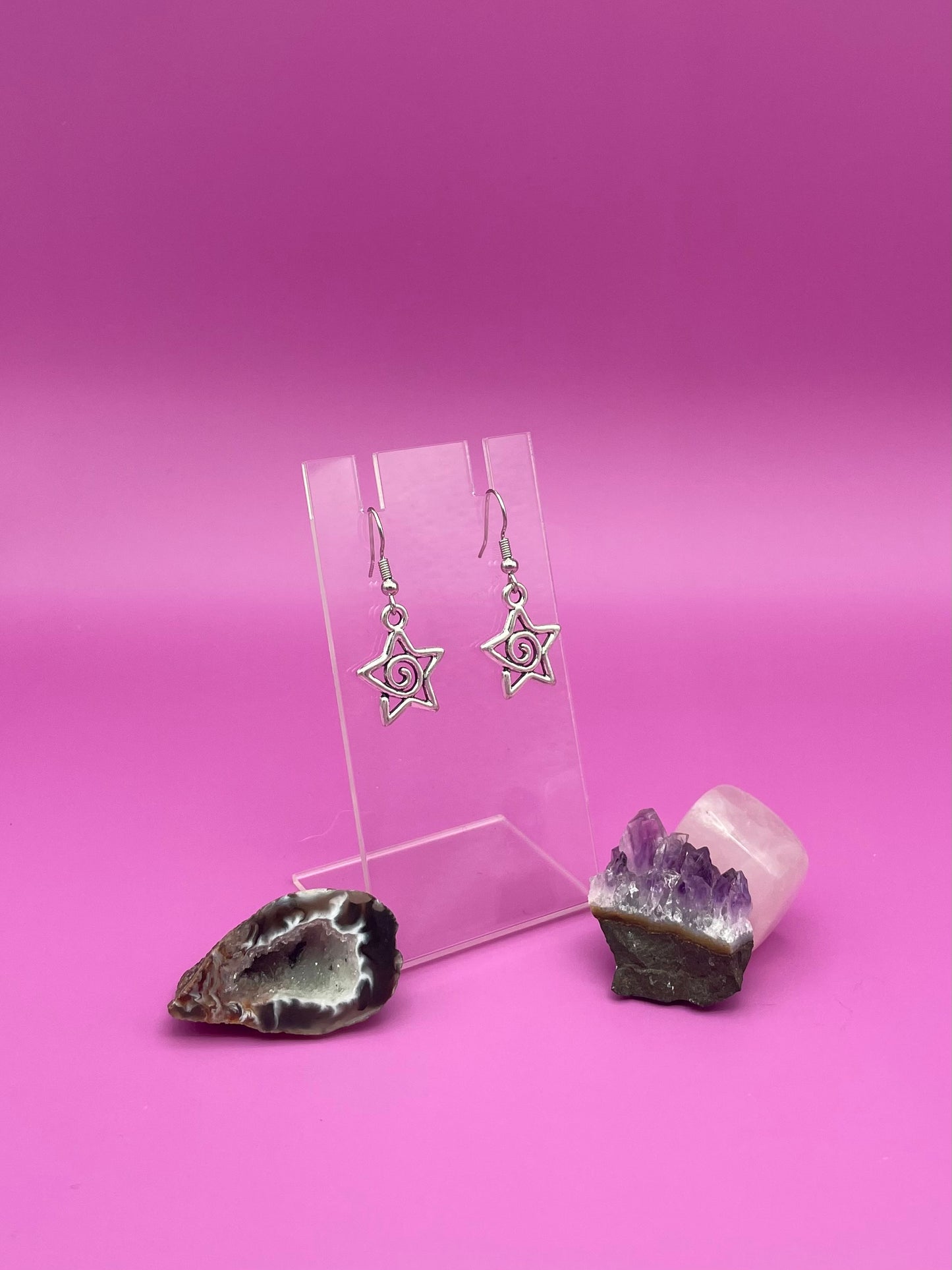 Silver Star-shaped swirl earrings on a clear stand with purple background