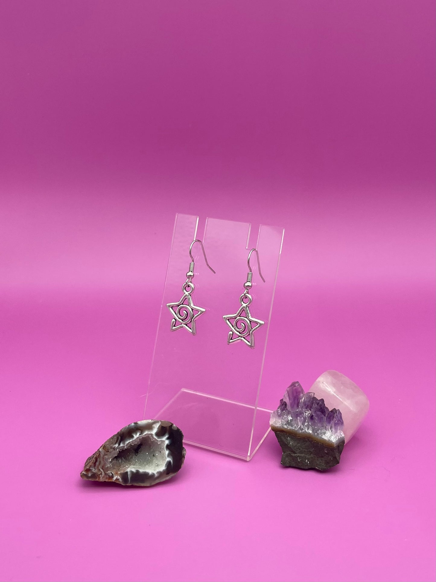 Silver Star-shaped swirl earrings on a clear stand with purple background