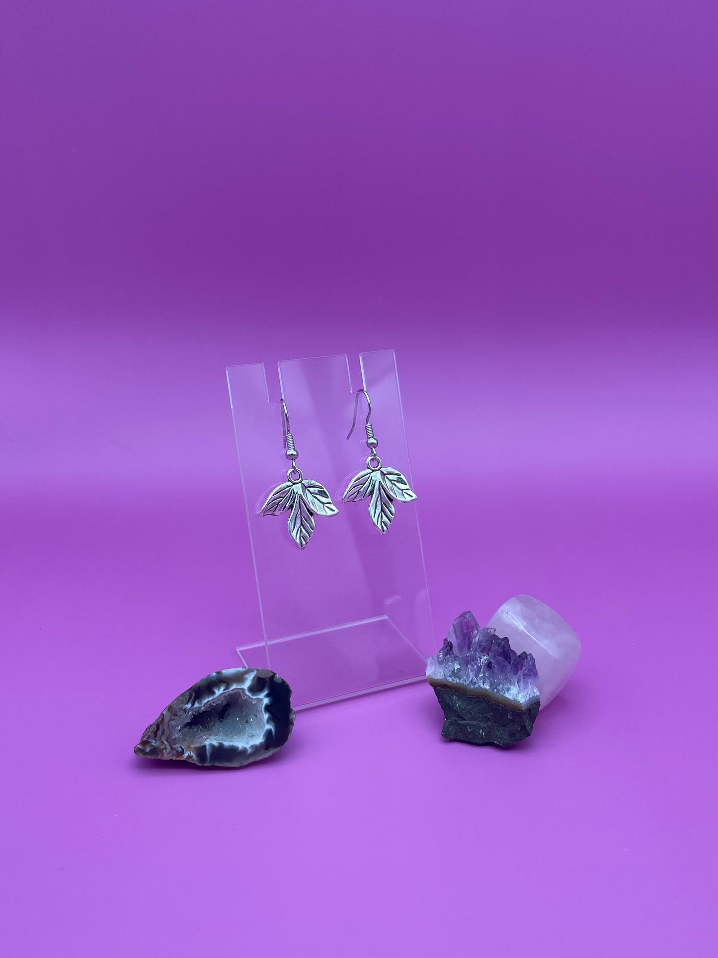 Silver leaf earrings on a clear stand with purple background