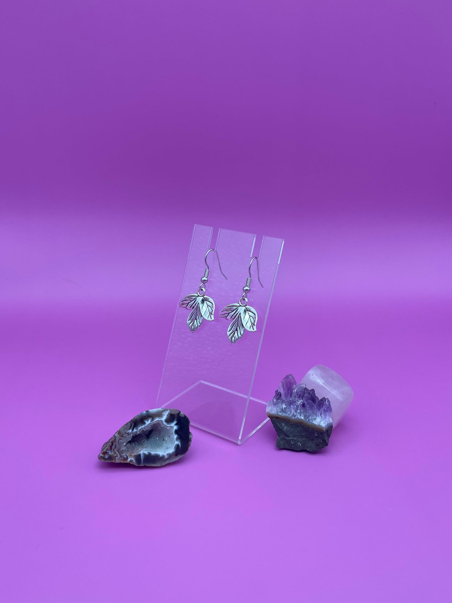 Silver leaf earrings on a clear stand with purple background