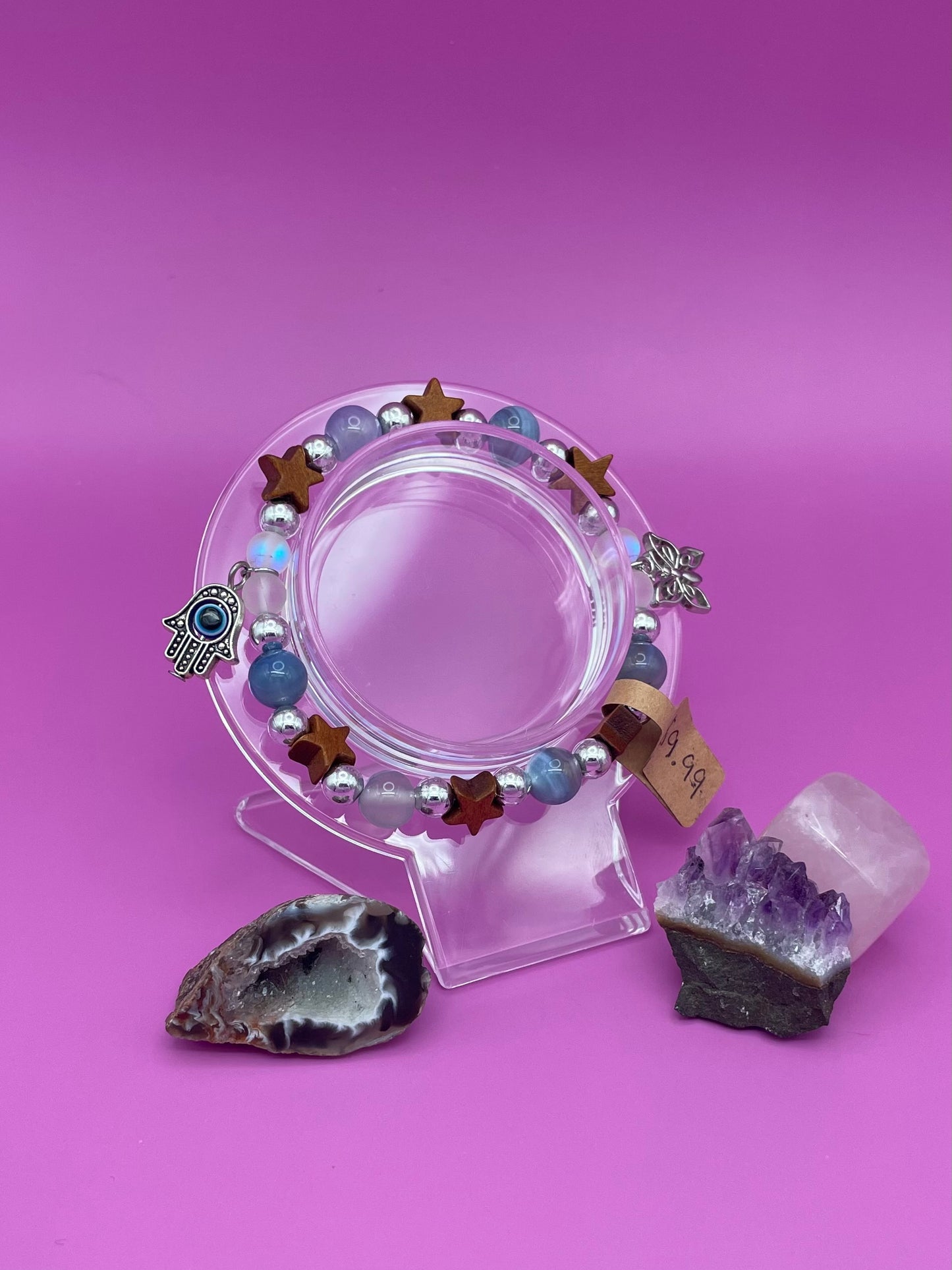 Bracelet with blue lace agate, wooden stars, and aura beads as well as two charms hanging on sides. A butterfly and an evil eye pendant, both silver.