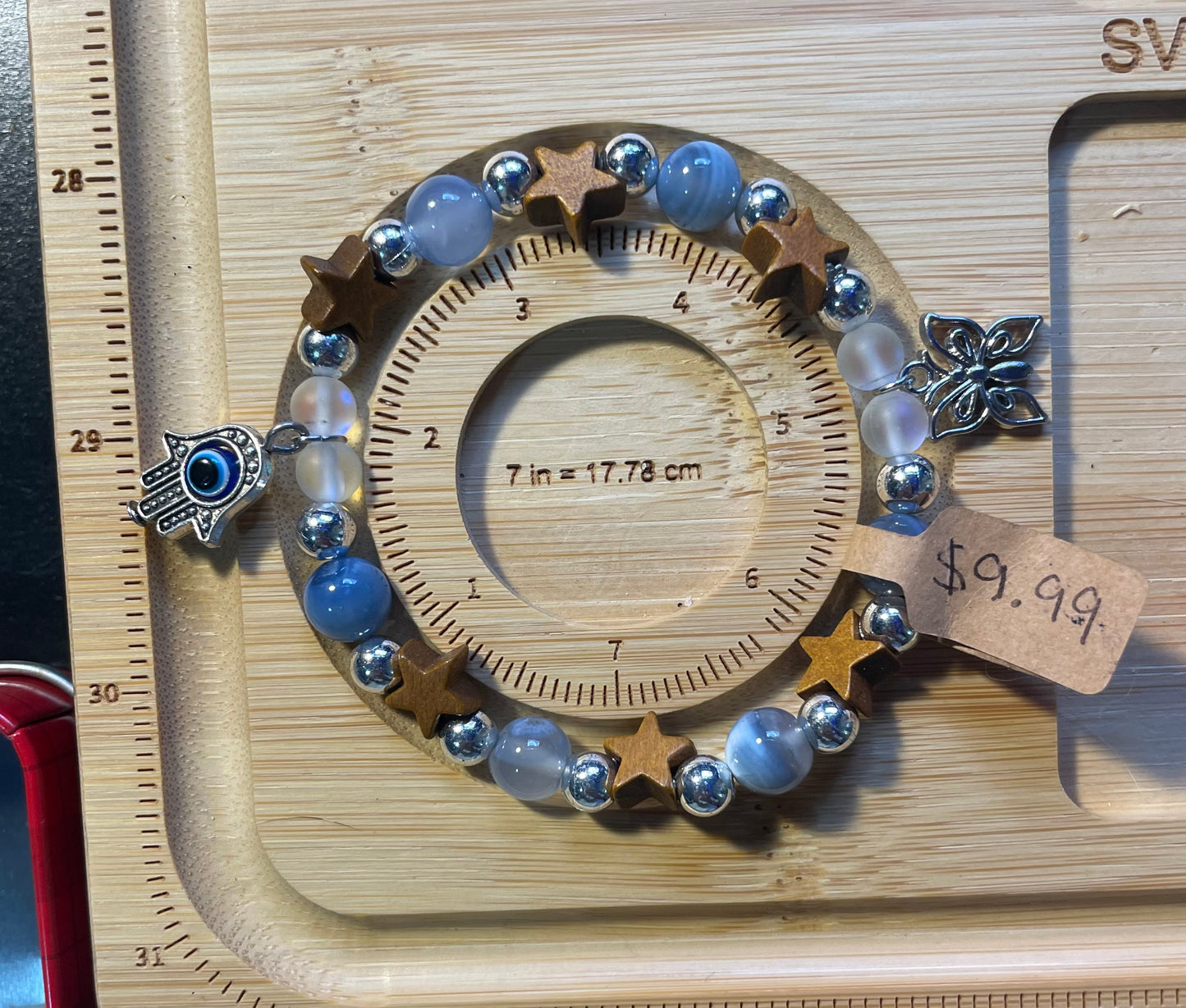 Bracelet with blue lace agate, wooden stars, and aura beads as well as two charms hanging on sides. A butterfly and an evil eye pendant, both silver.