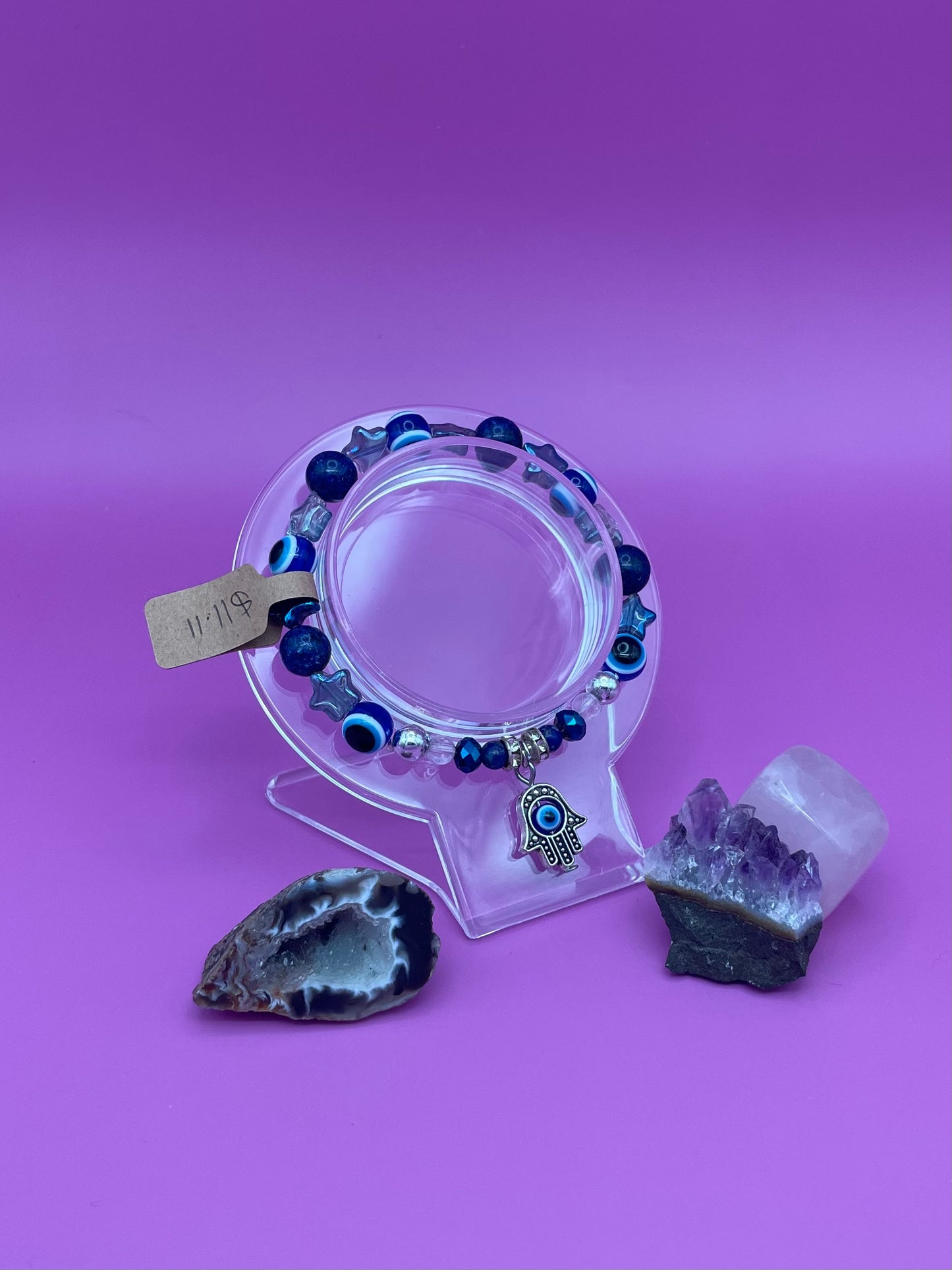 Bracelet with blue beads and Hamsa hand charm on a clear stand with crystals on a purple background