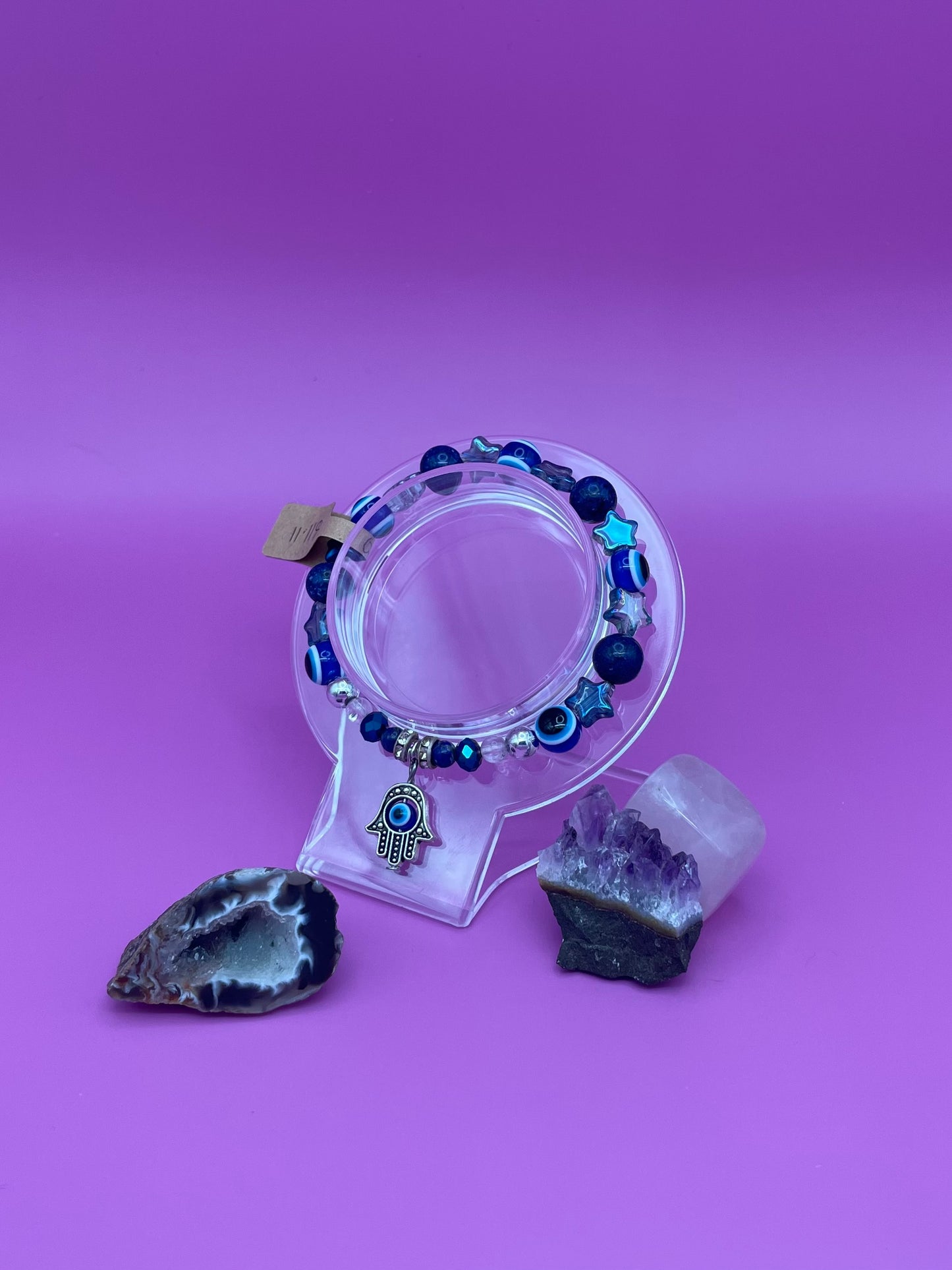 Bracelet with blue beads and Hamsa hand charm on a clear stand with crystals on a purple background