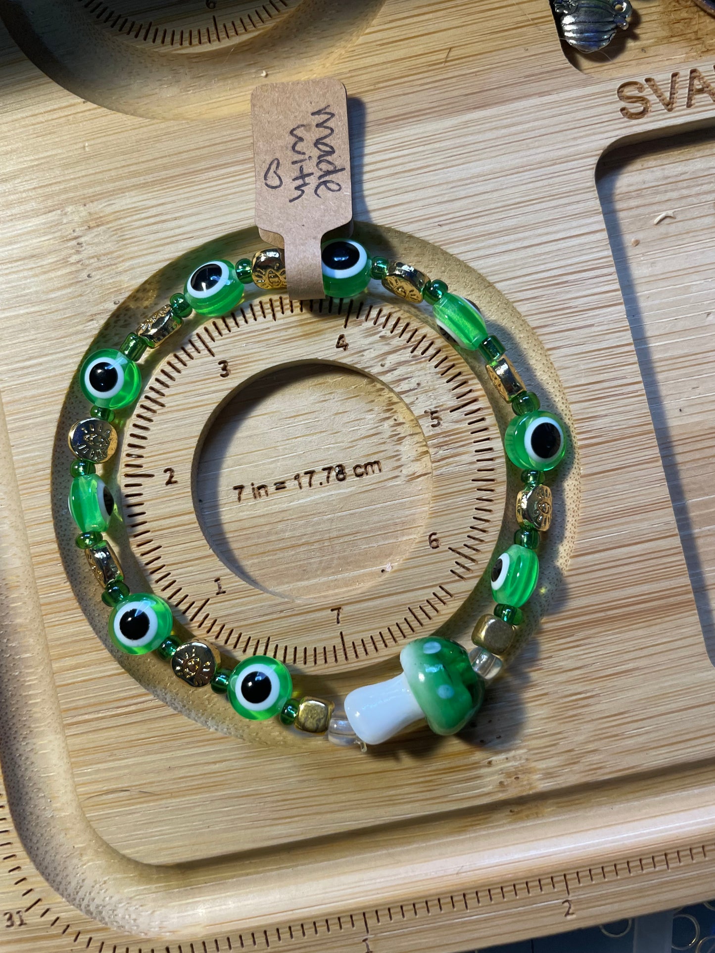 Bracelet with green evil eye beads and main glass green mushroom bead on a wooden sizing board 7in