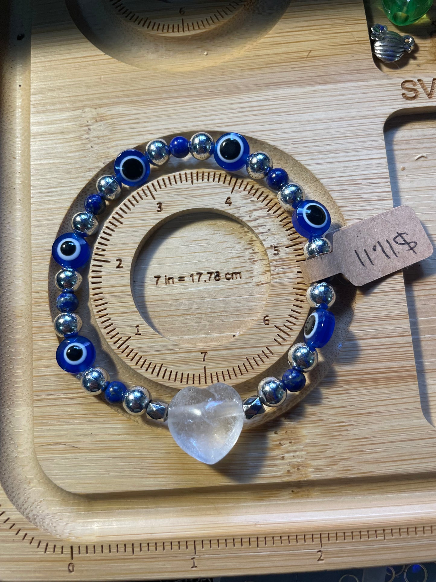 Blue and silver evil eye bracelet with clear quartz crystal centerpiece on wooden sizing board, 7inches