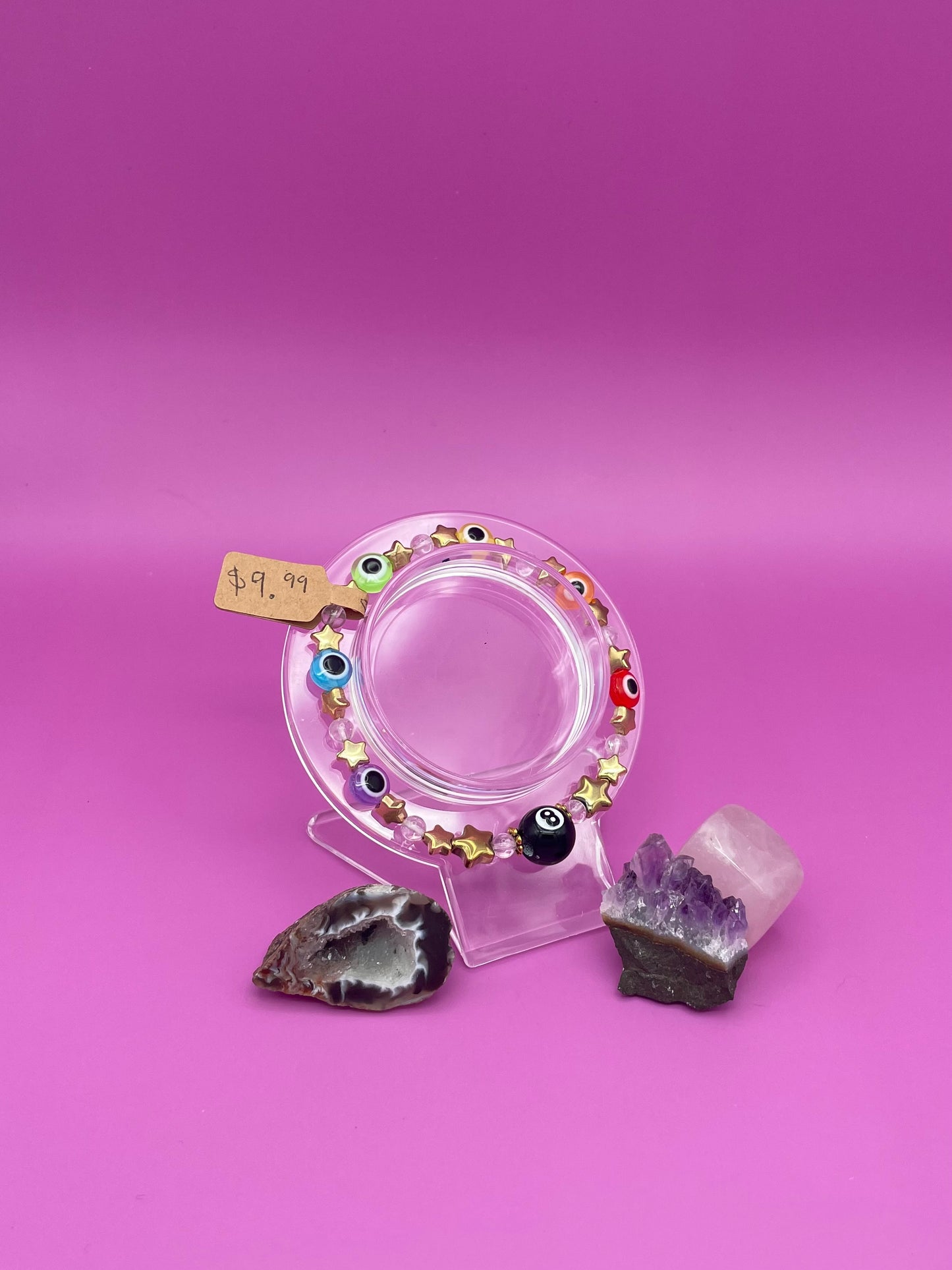 Bracelet with evil eye rainbow beads, gold stars, and clear quartz beads in a pattern with a black 8ball as the main center piece
