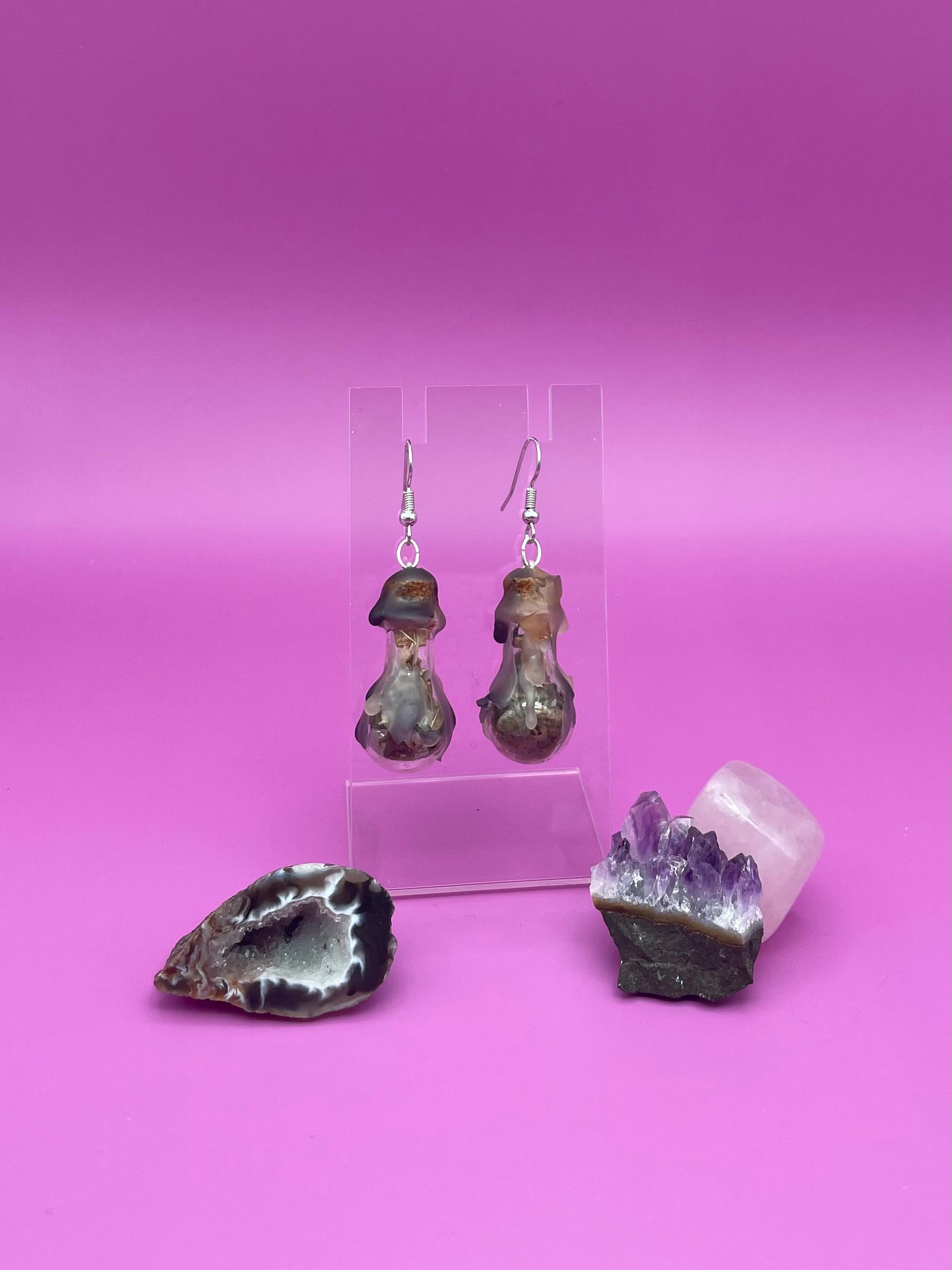 Protection spell earrings on clear stand with purple background