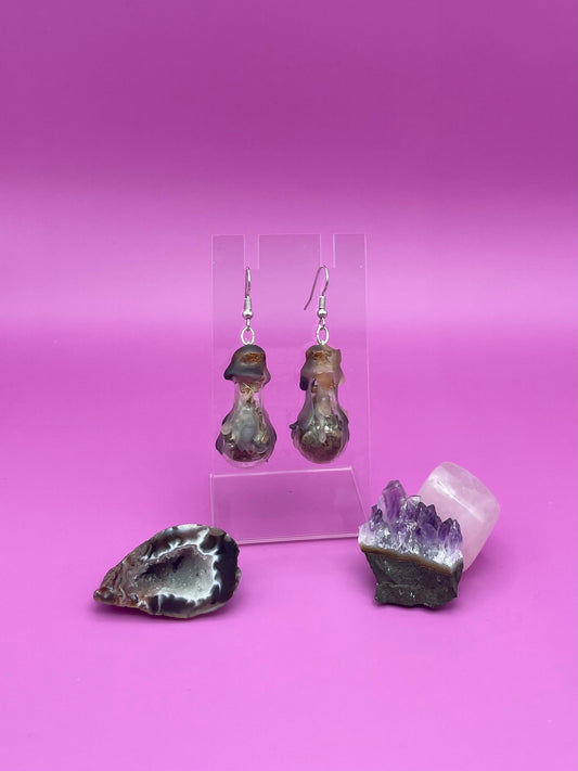 Protection spell earrings on clear stand with purple background
