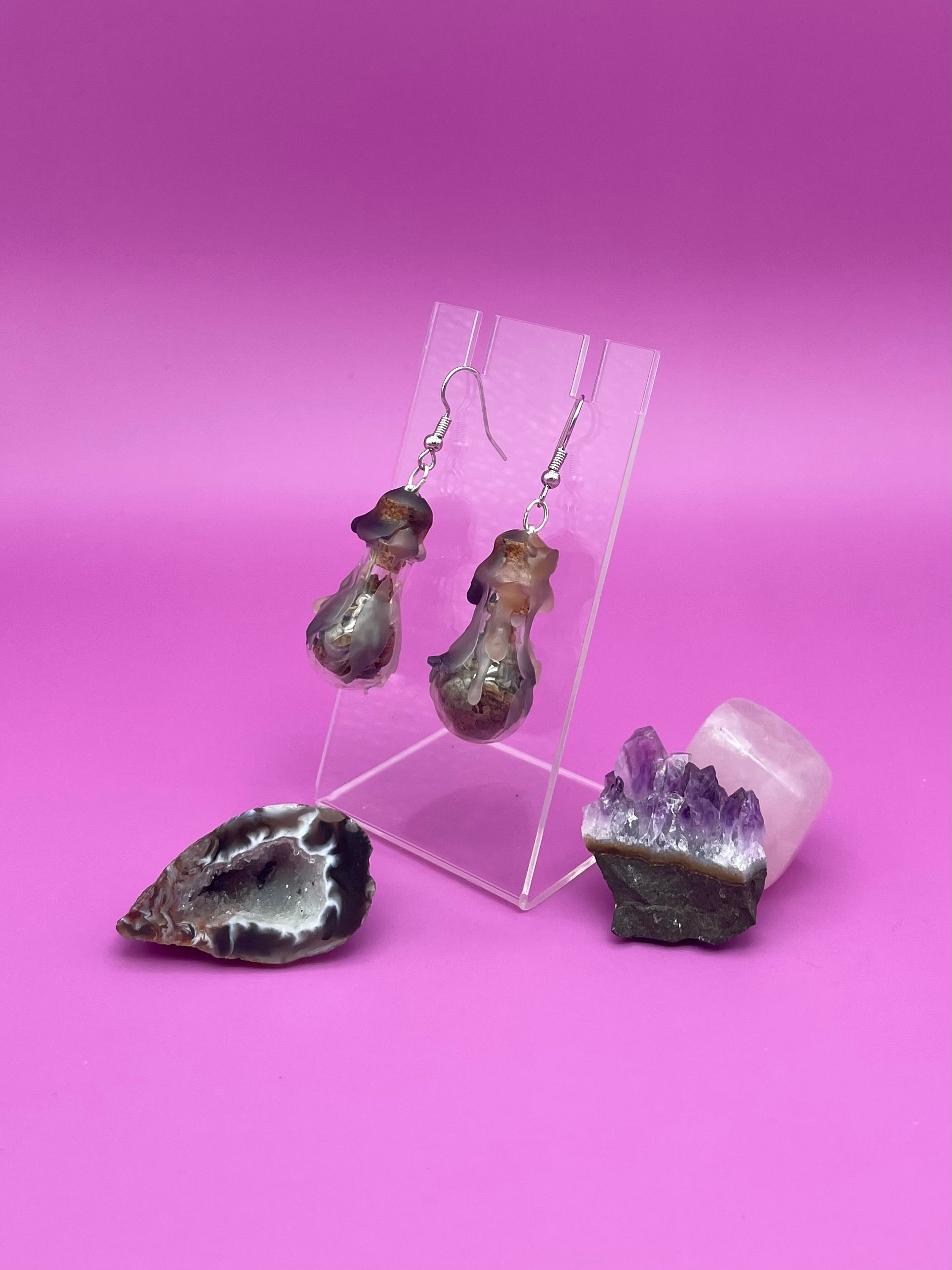 Protection spell earrings on clear stand with purple background