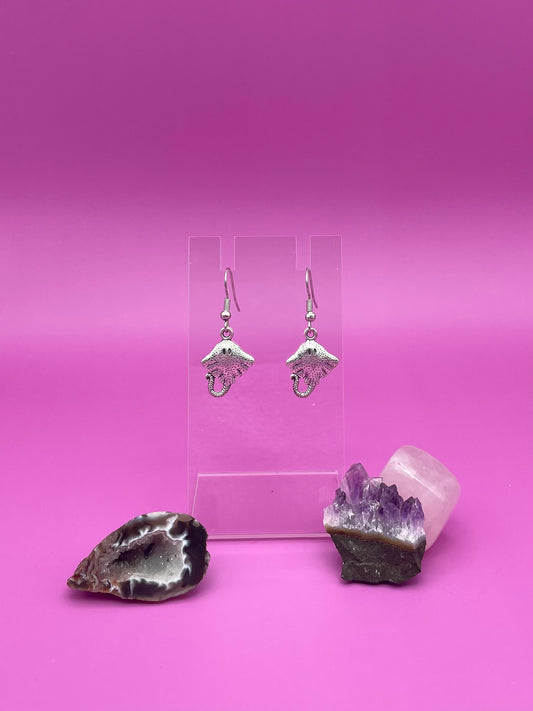 Silver stingray earrings on clear stand purple background