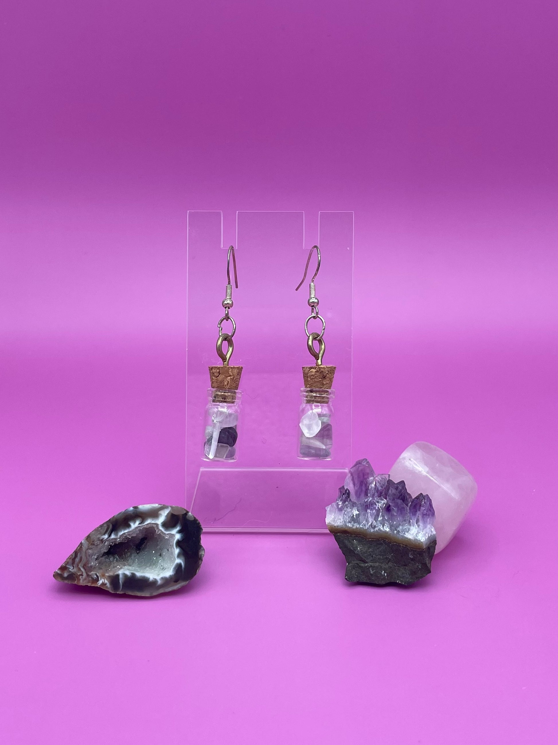 Fluorite filled jar earrings on a clear stand with crystals on a pink background