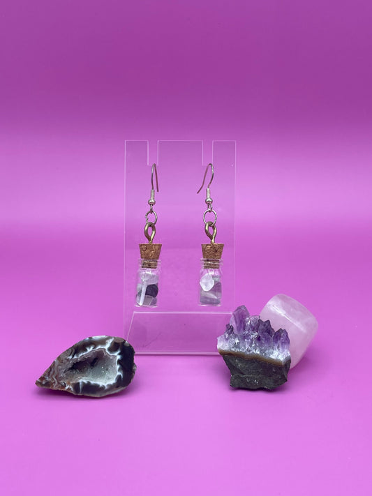 Fluorite filled jar earrings on a clear stand with crystals on a pink background