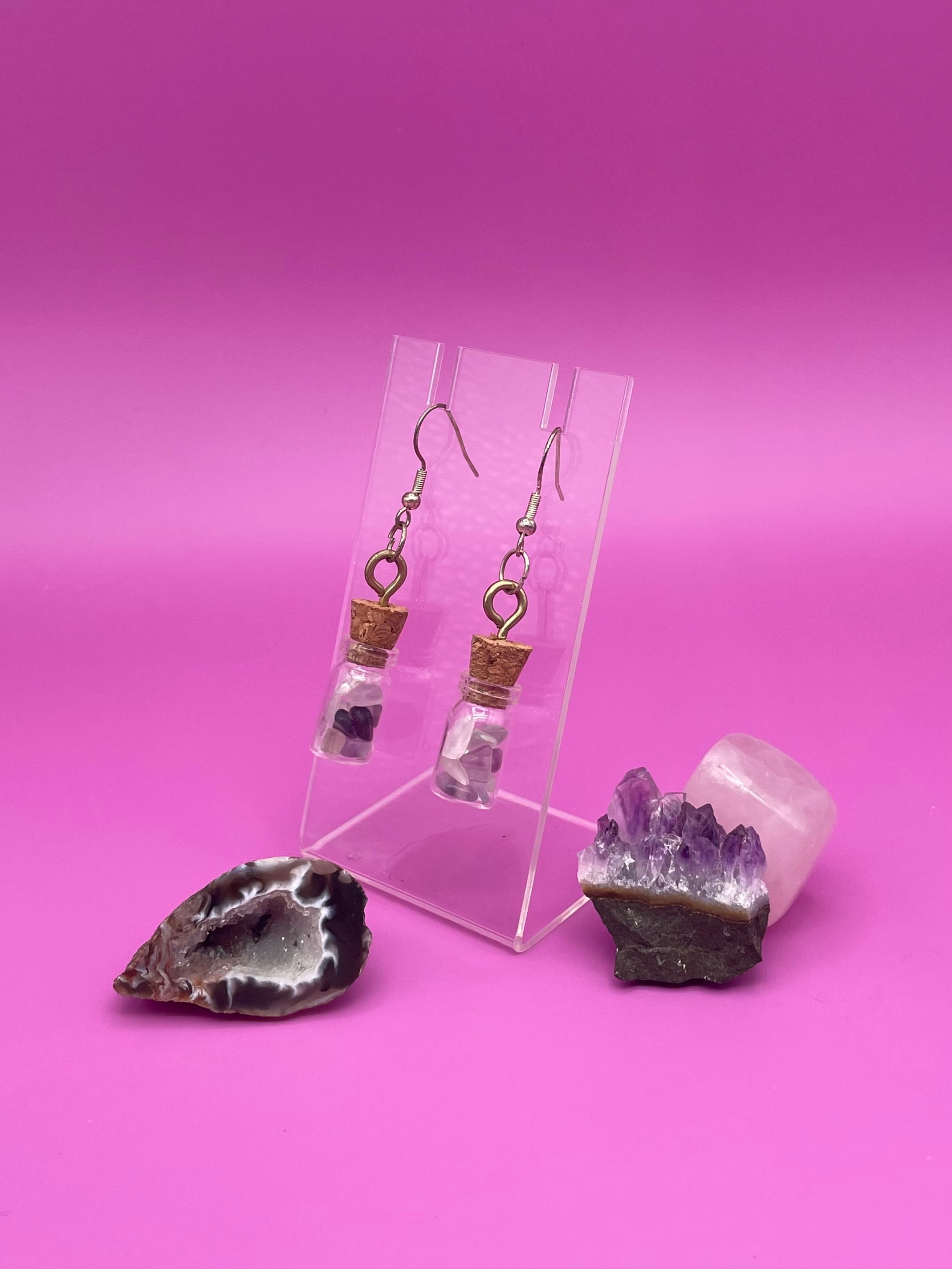 Fluorite filled jar earrings on a clear stand with crystals on a pink background