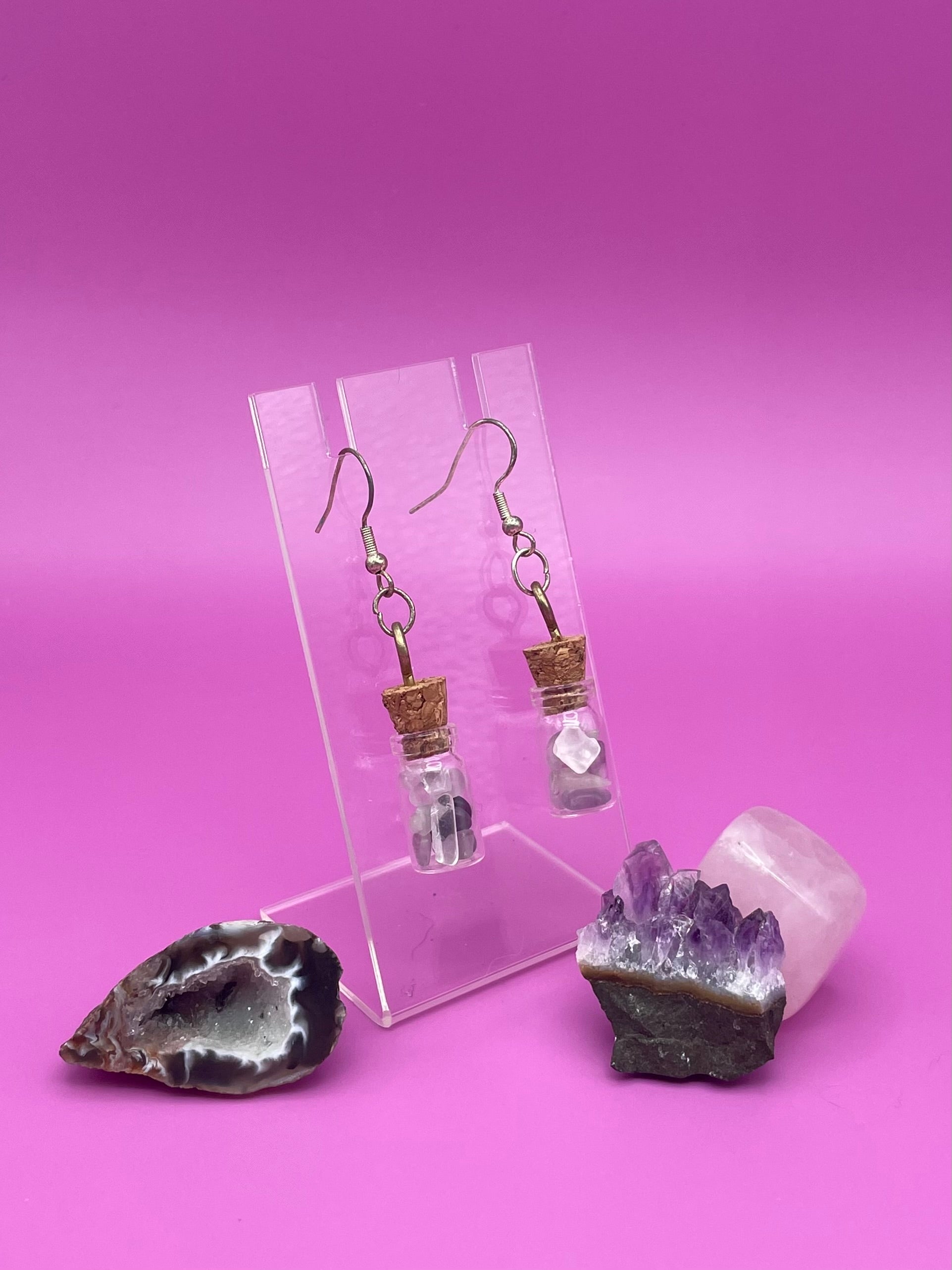 Fluorite filled jar earrings on a clear stand with crystals on a pink background