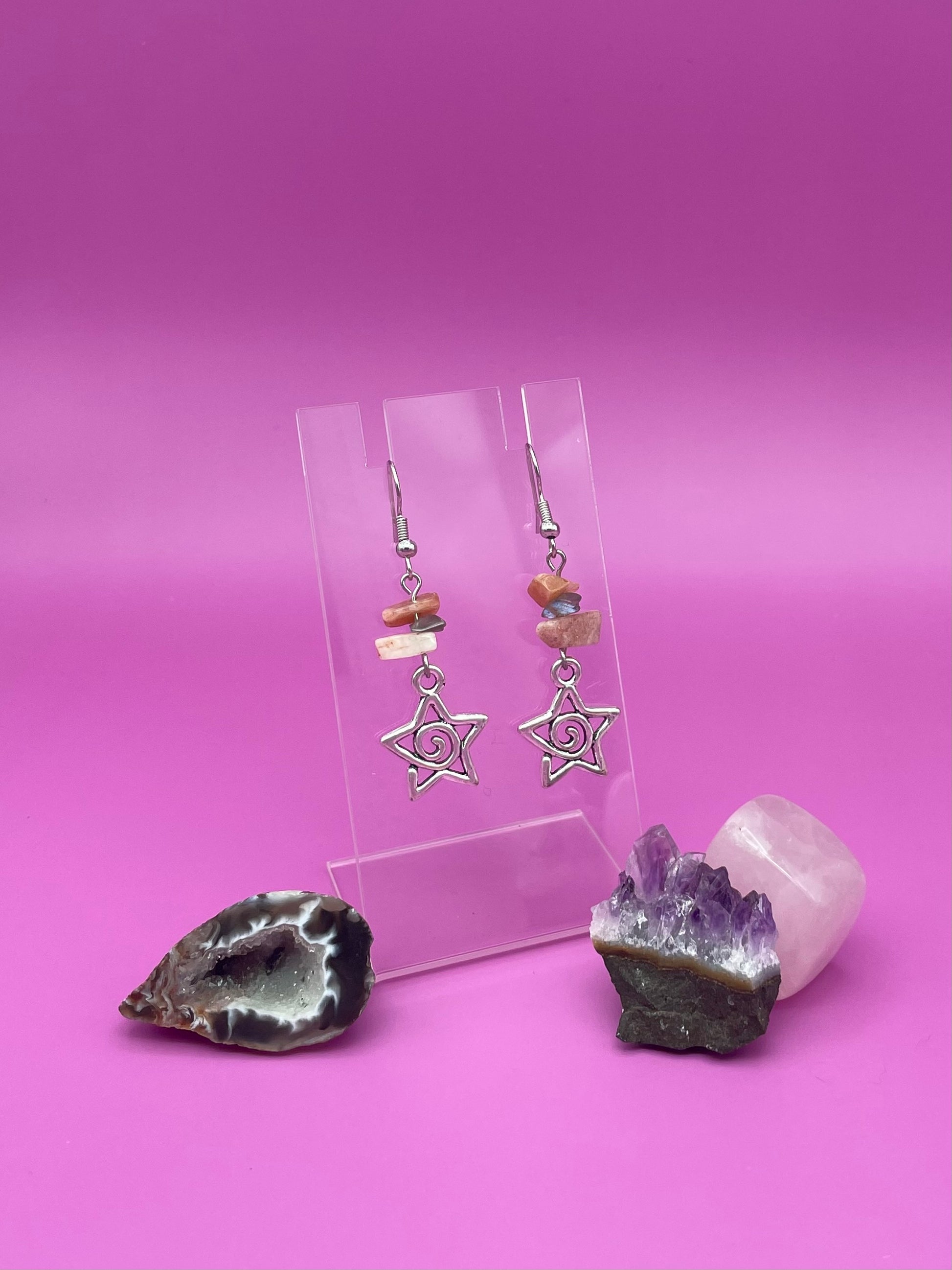 Star-shaped swirl earrings on a clear stand with amethyst crystal and a purple background