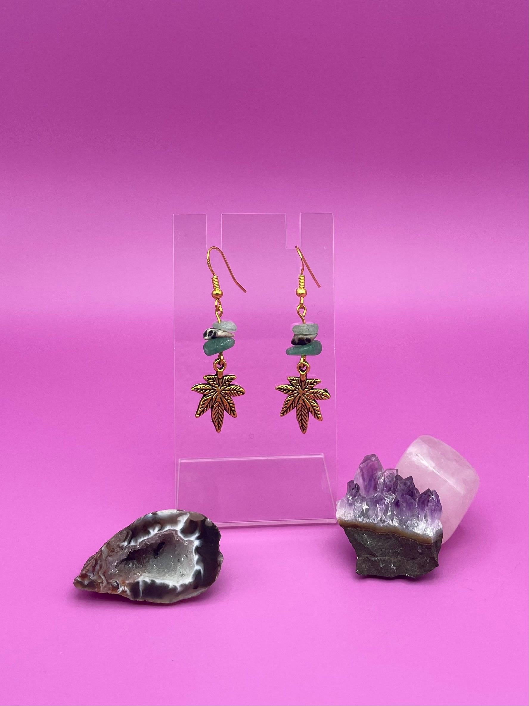 Gold leaf charm with crystal chips earrings on a clear stand with amethyst crystal on a pink background