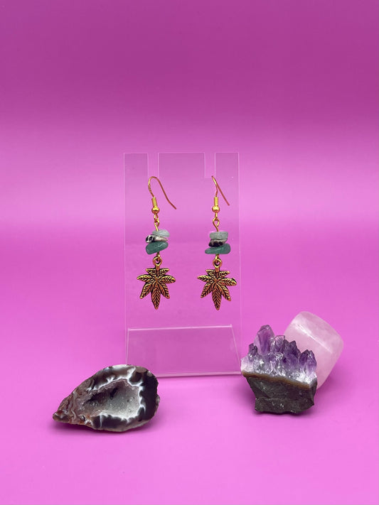 Gold leaf charm with crystal chips earrings on a clear stand with amethyst crystal on a pink background