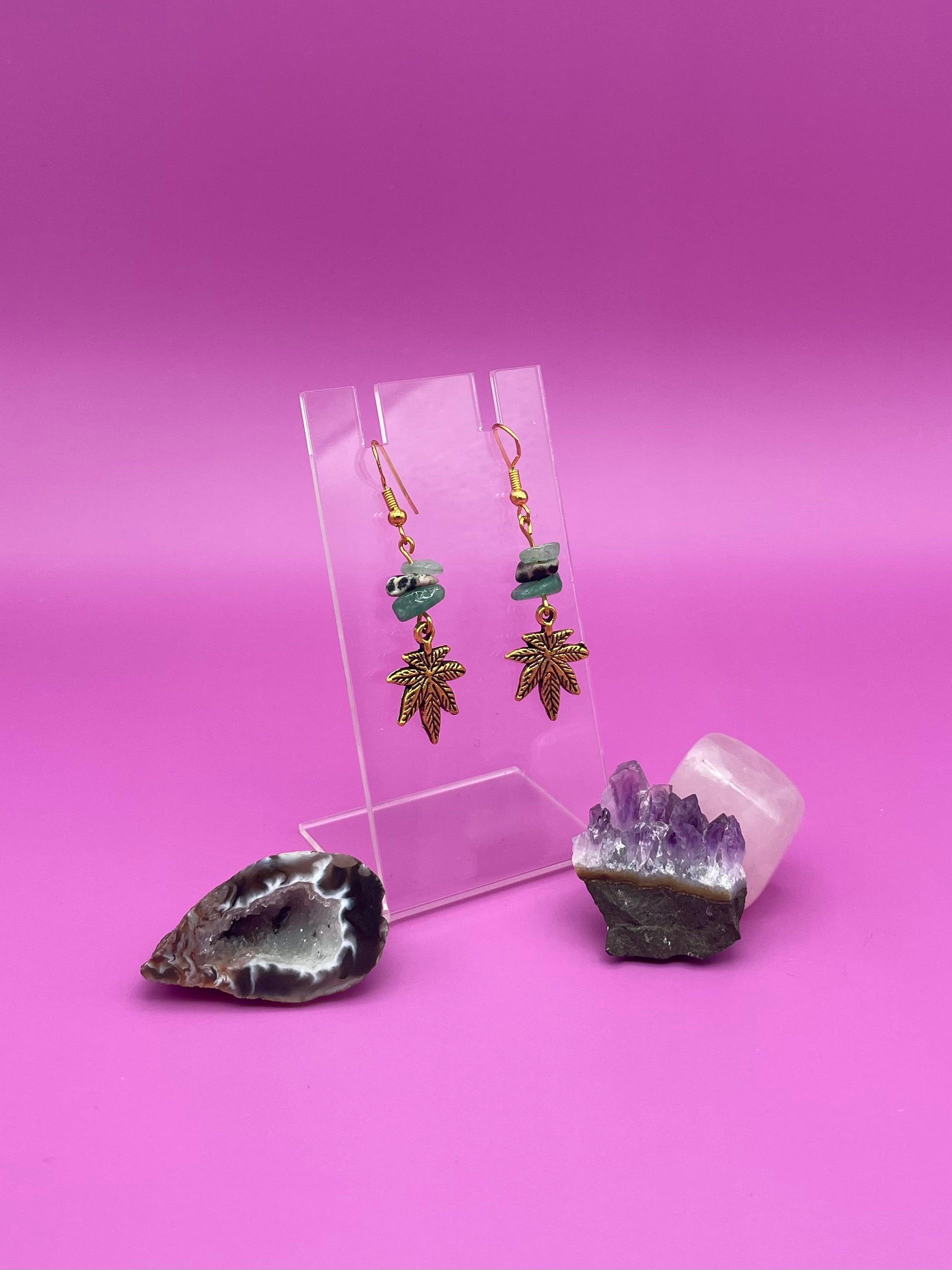 Gold leaf charm with crystal chips earrings on a clear stand with amethyst crystal on a pink background