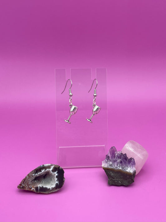 Silver wine glass earrings on a clear stand with purple background